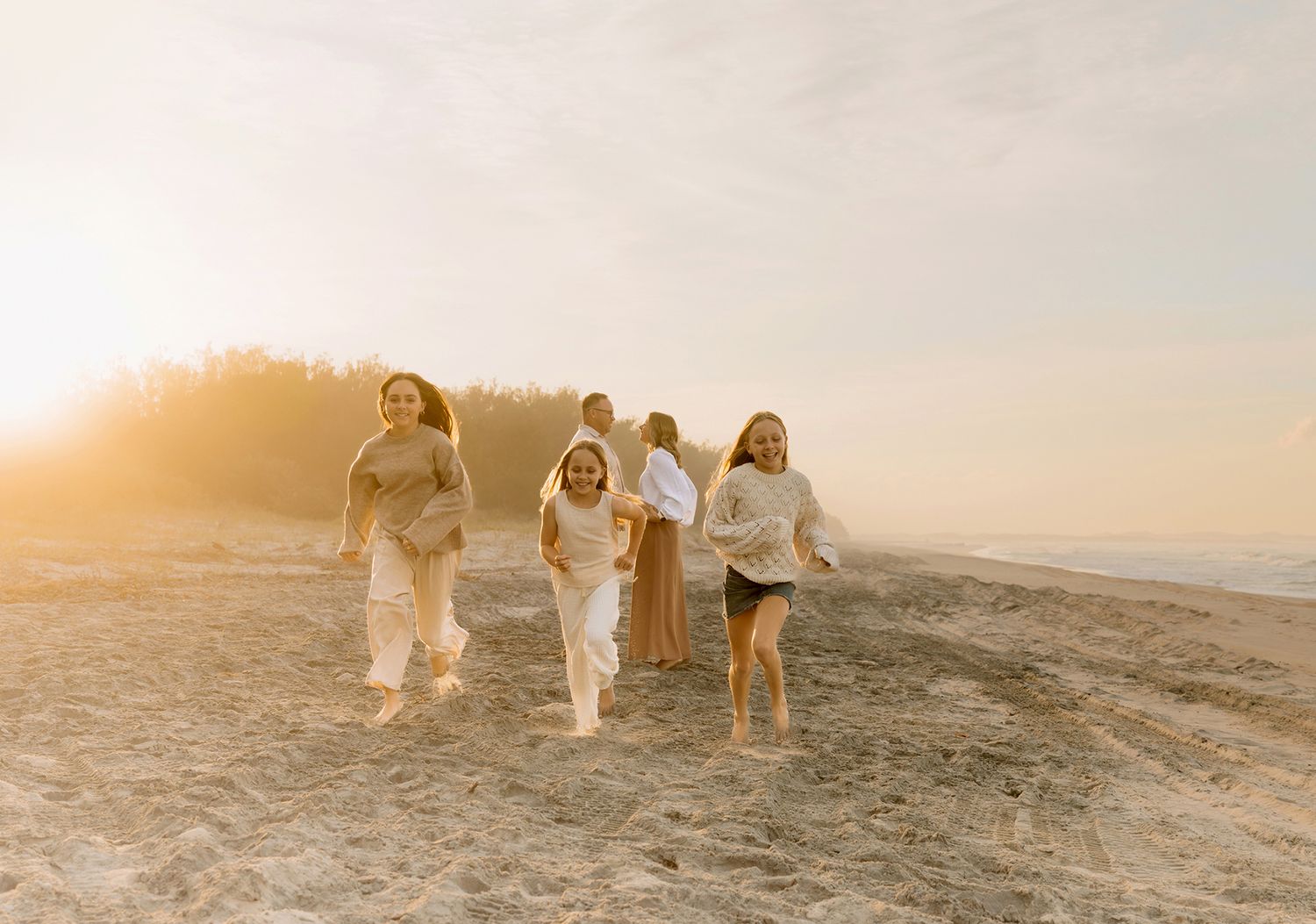 A family playfully walk along a sandy beach during sunset creating a dreamy coastal photo shoot at Stradbroke Island.