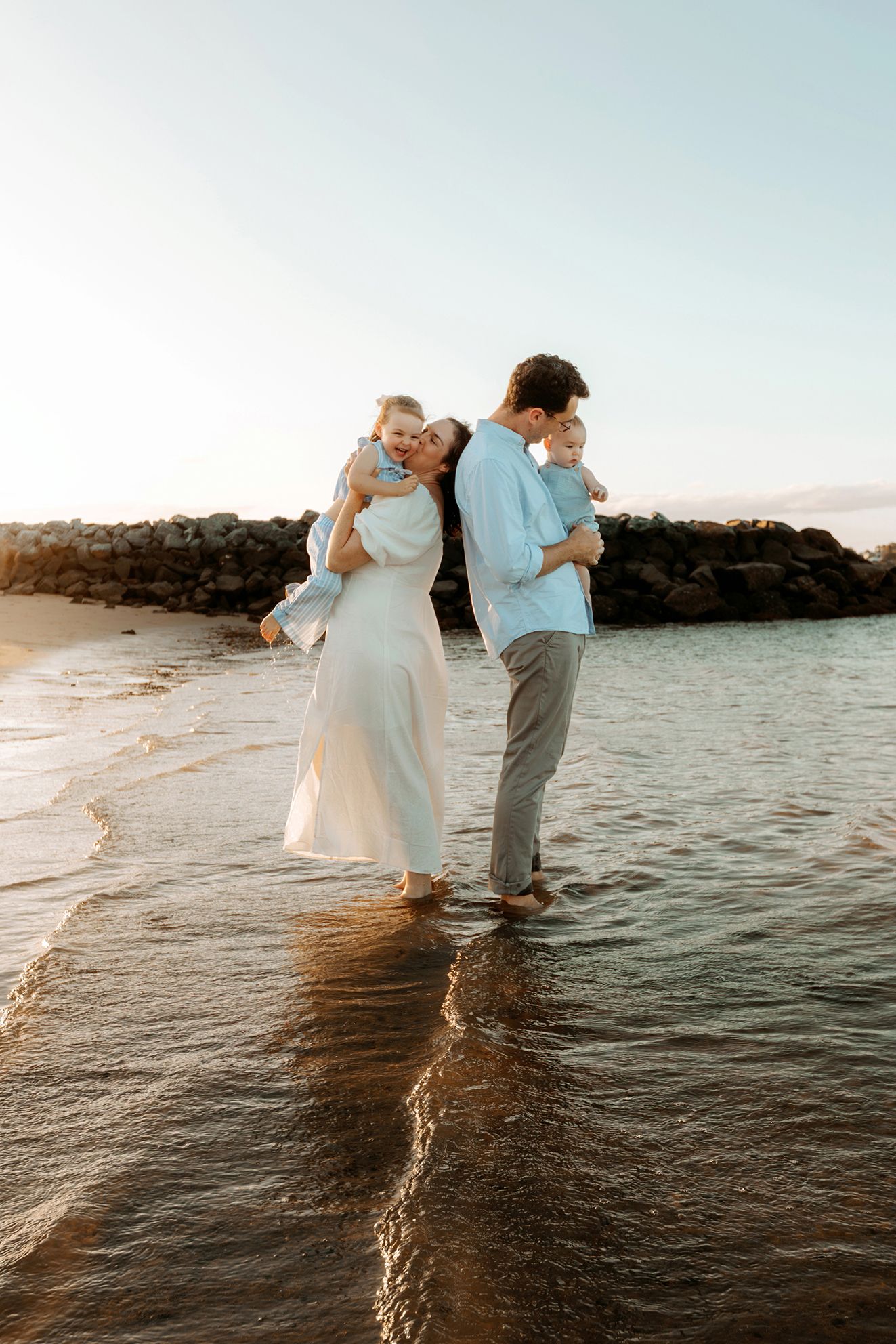 Family photoshoot at Raby Bay beach with golden lighting in water at sunset.