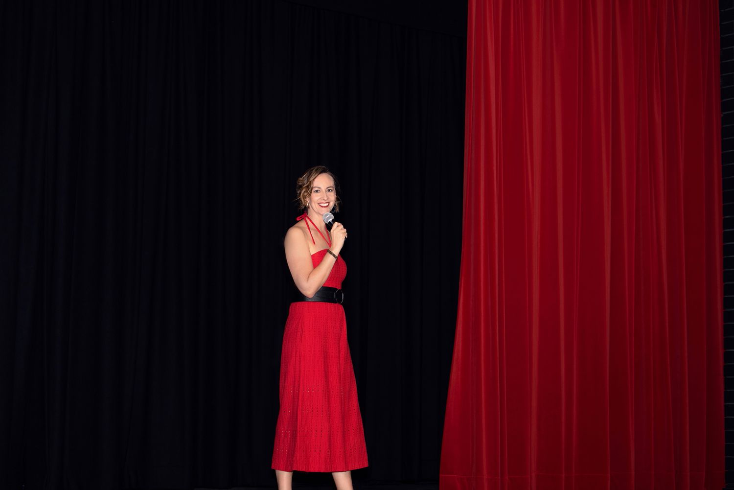 Photography of silhouette of performer against red stage curtain background.