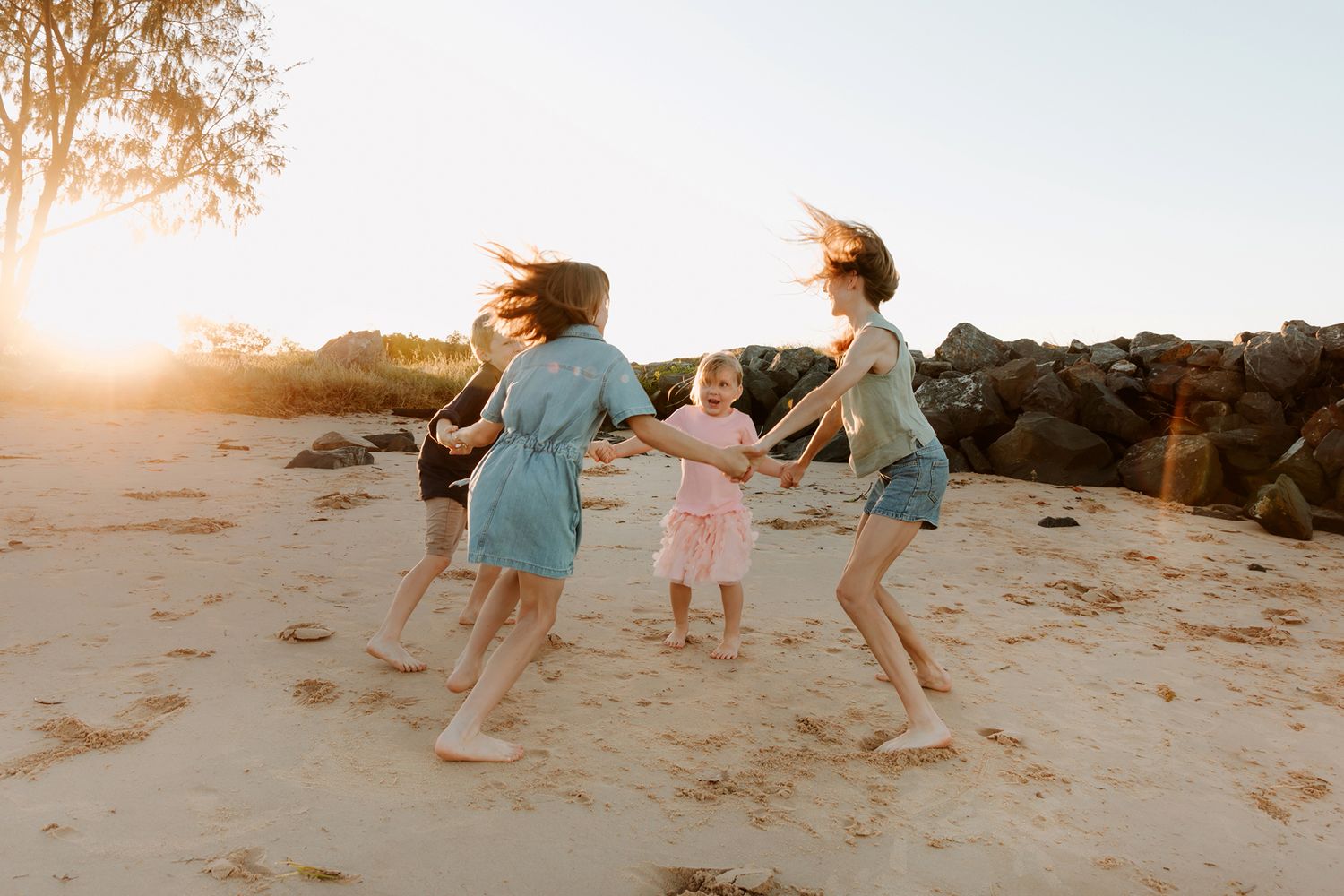 Siblings run and play on a sandy beach with rocks in the background during golden hour at Brisbane bayside beach.