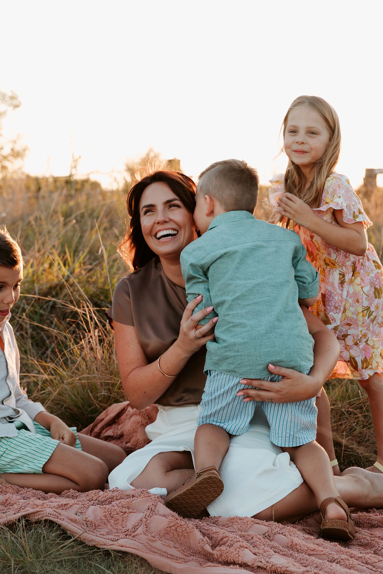 A family shares a joyful moment together while sitting on a blanket for a photo shoot in a grassy field at Mt Cotton, Brisbane.