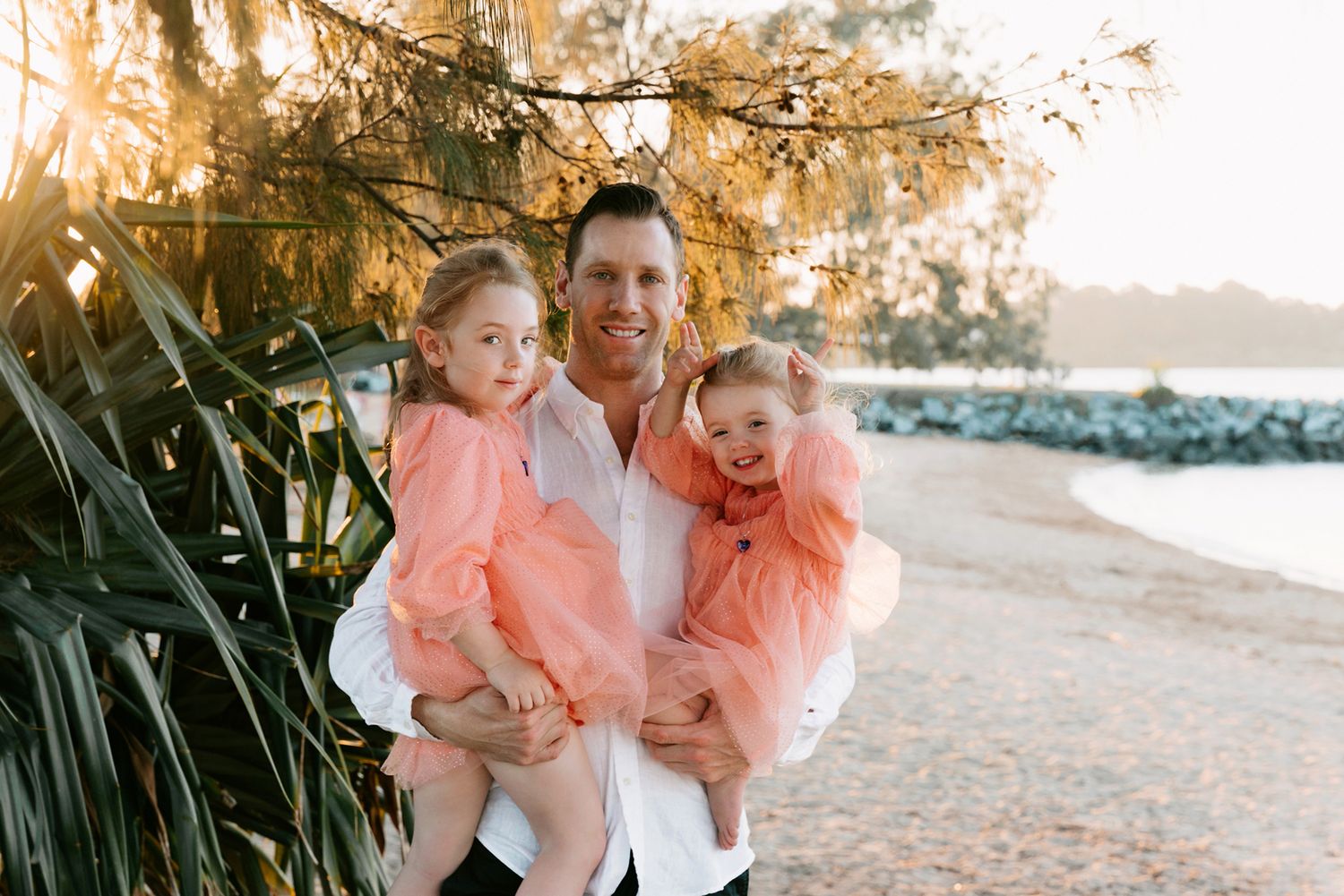 Candid family photography captured at sunset with palm trees and the bayside in the background at Raby Bay Foreshore, Cleveland, Redlands.