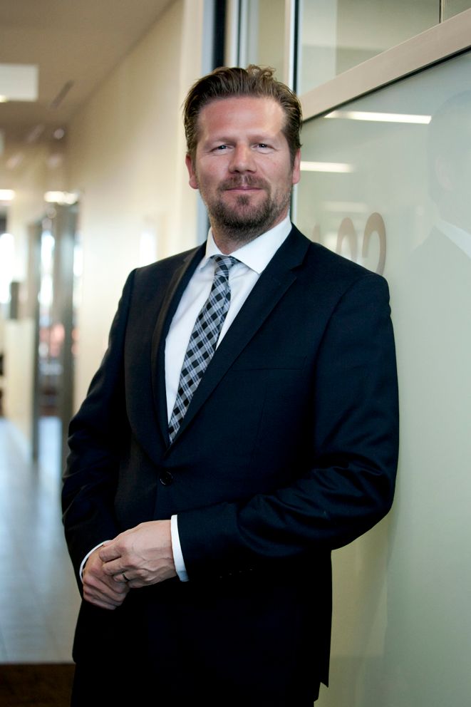 Brisbane corporate photography show casing a professional wearing a black suit and checkered tie stands in a bright office hallway.