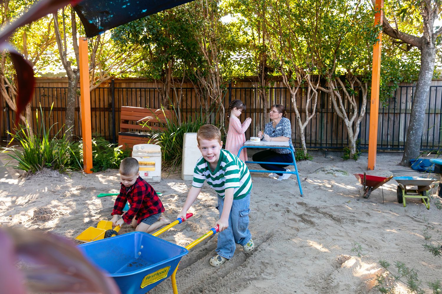 Children play on outdoor playground equipment under shaded tree canopy of Brisbane kindergarten for business photography.