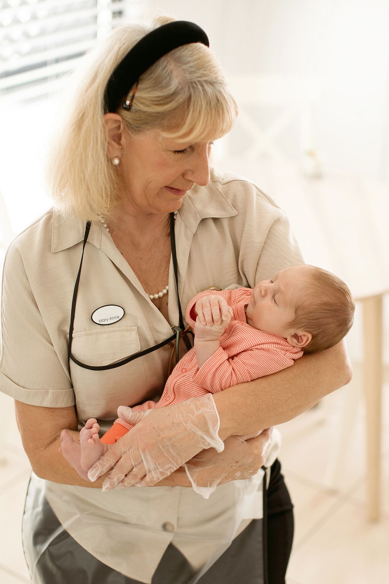 Brisbane business photographer illustrating healthcare professional in beige uniform holding and comforting a small infant.