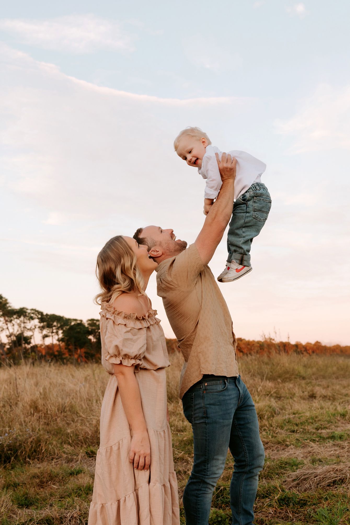 Playful family photography is captured in a Brisbane field during sunset with warm natural lighting.