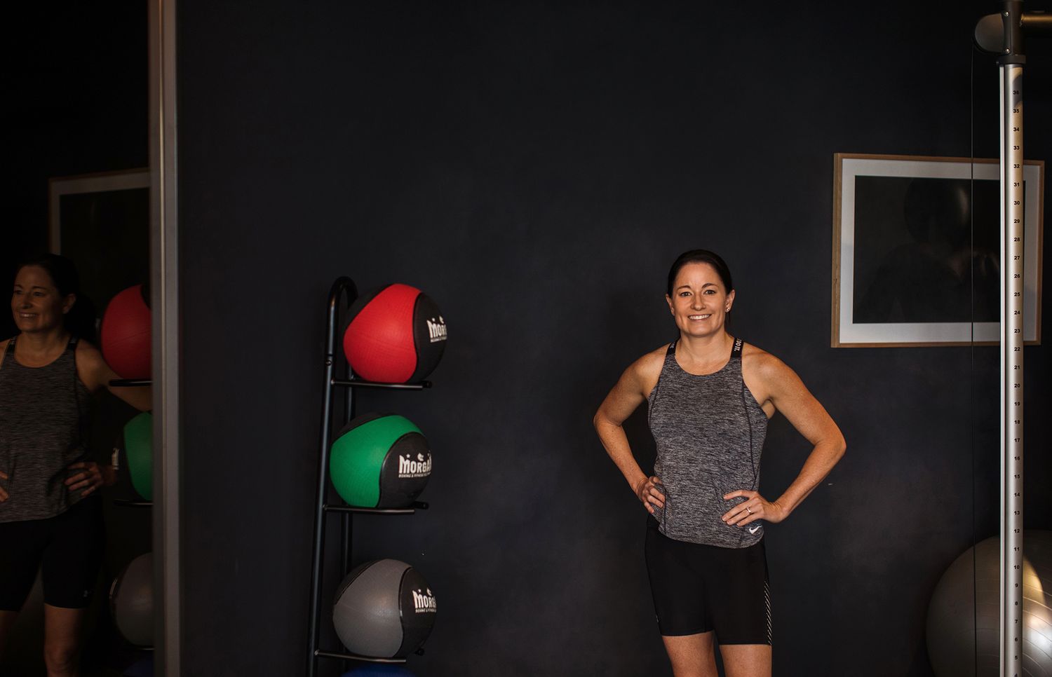 Brisbane business photographer illustrating gym photoshoot with participant posing against black wall with exercise equipment.
