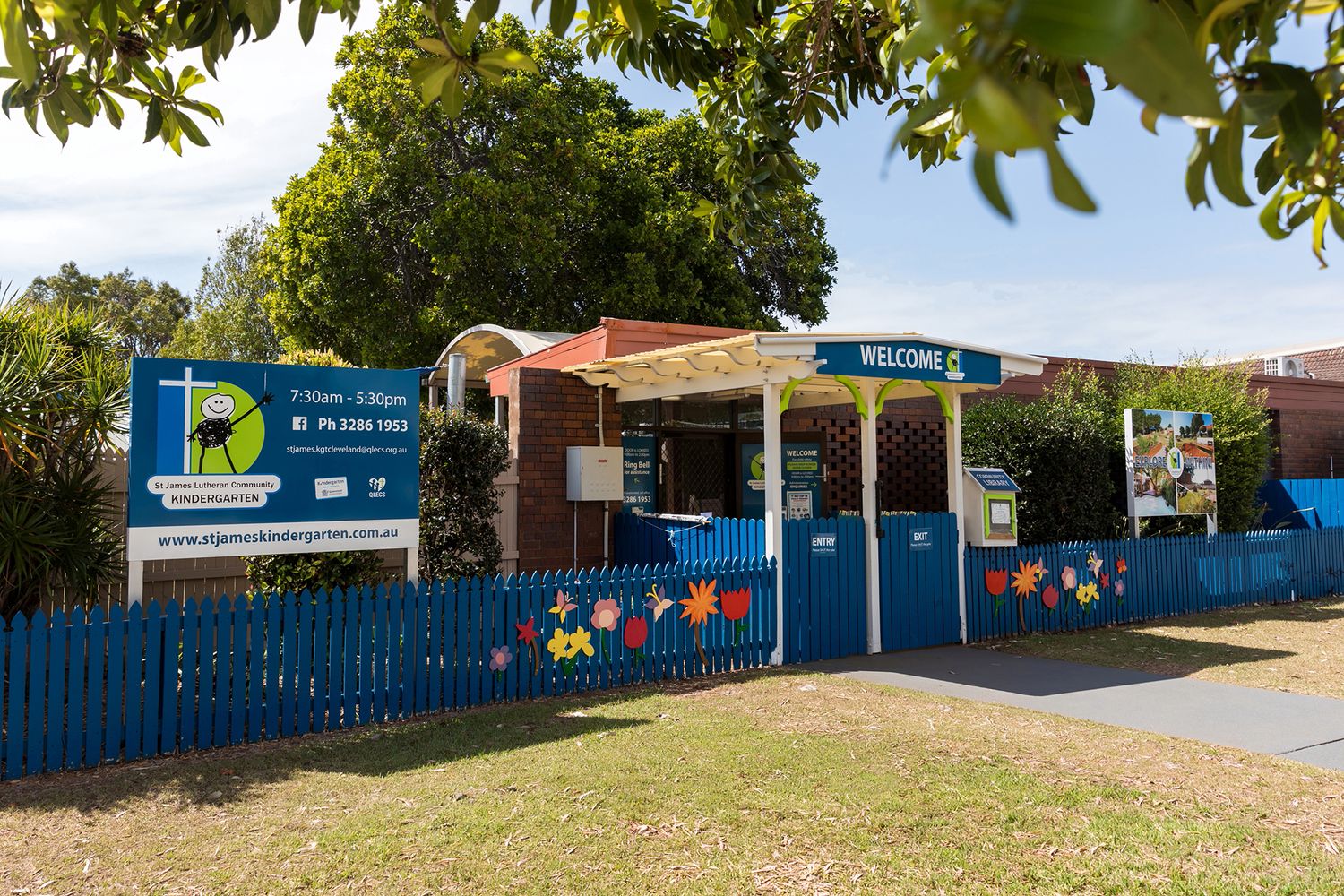 Kindergarten business photography showing a wide panoramic shot of the Brisbane daycare facility exterior with blue fencing and play area.