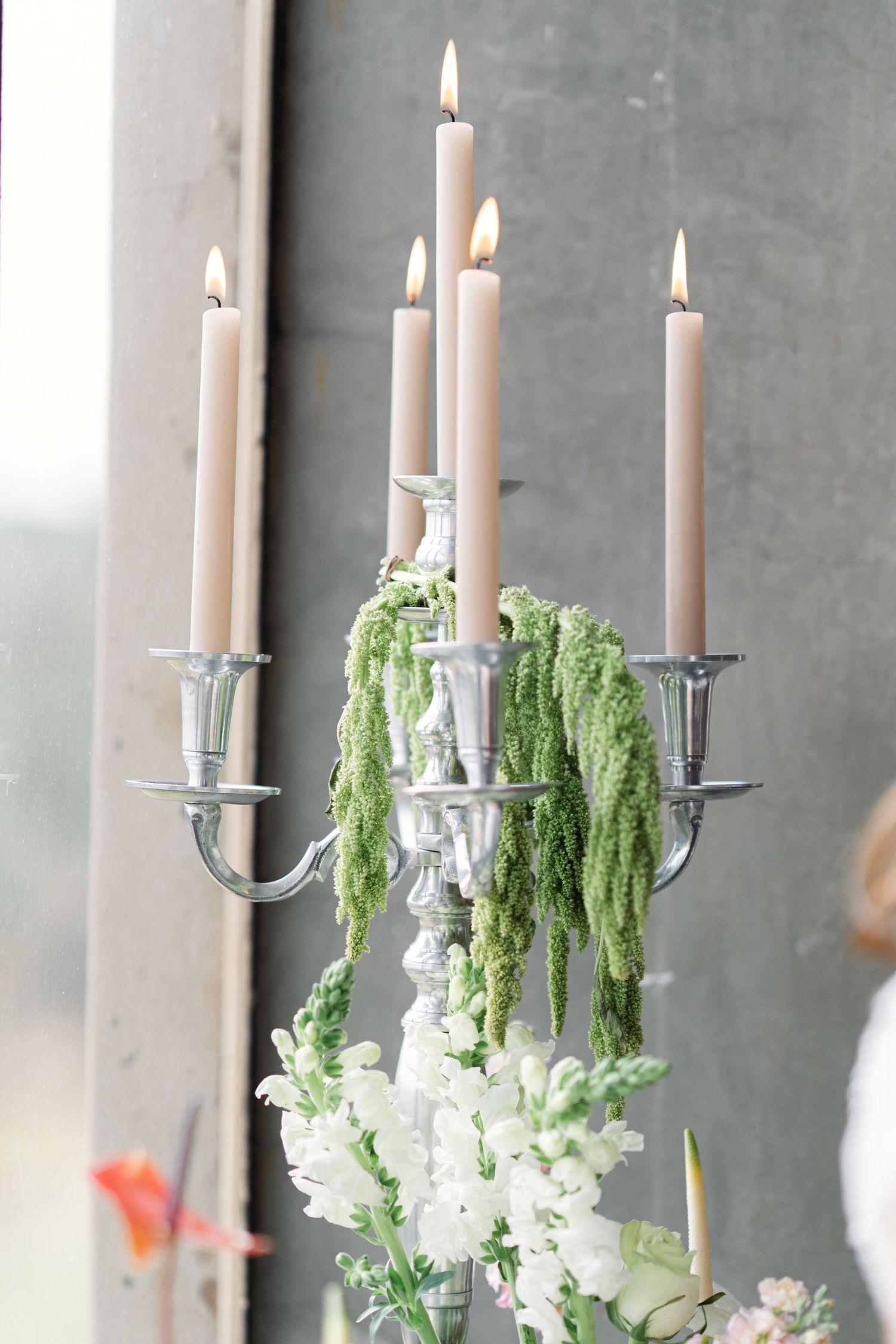 Elegant candelabras adorned with white candles and cascading greenery against a gray concrete wall create a romantic ambiance.