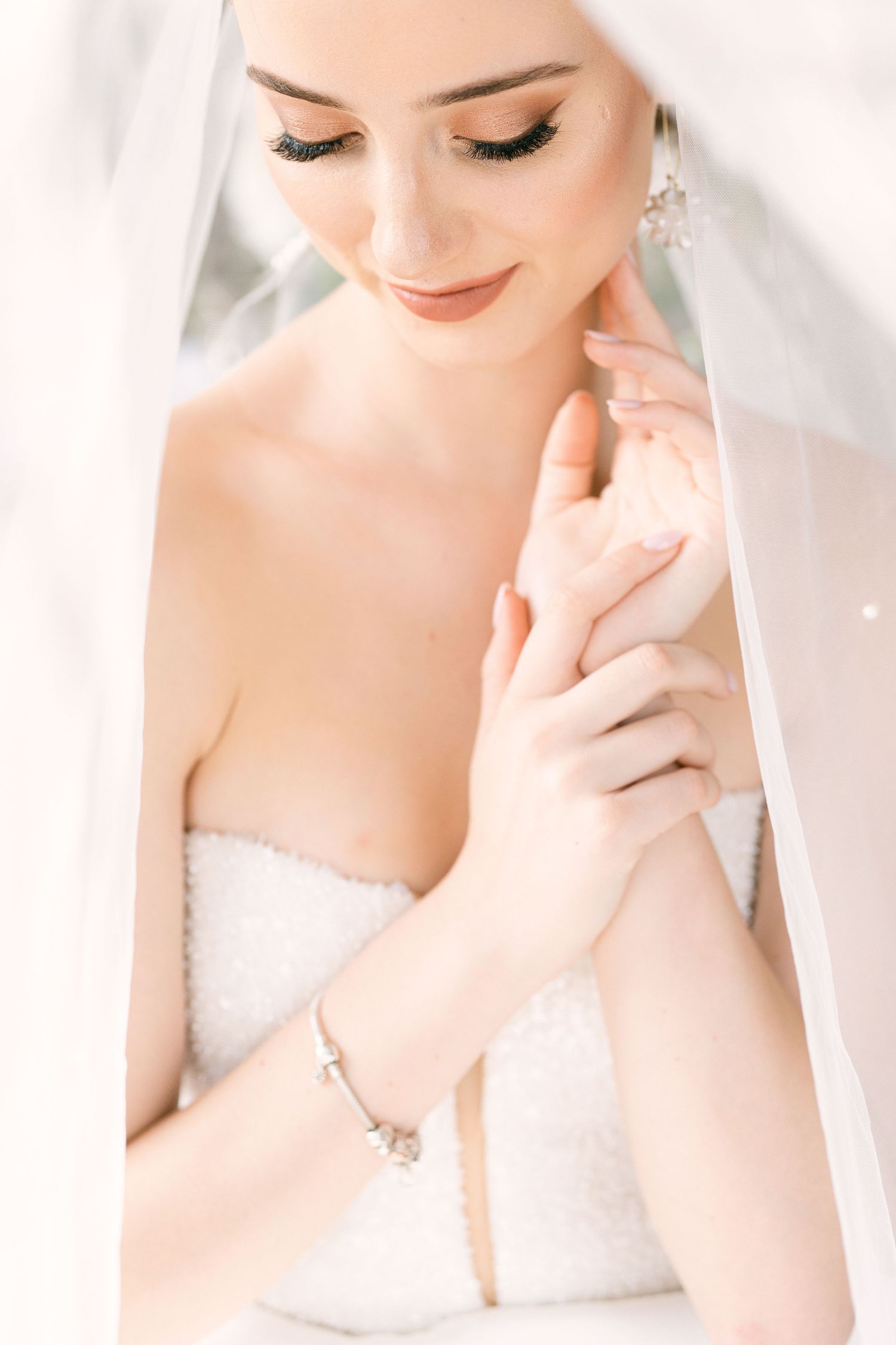 A bride in white poses gracefully in a soft, dreamy bridal portrait with elegant makeup and styling.