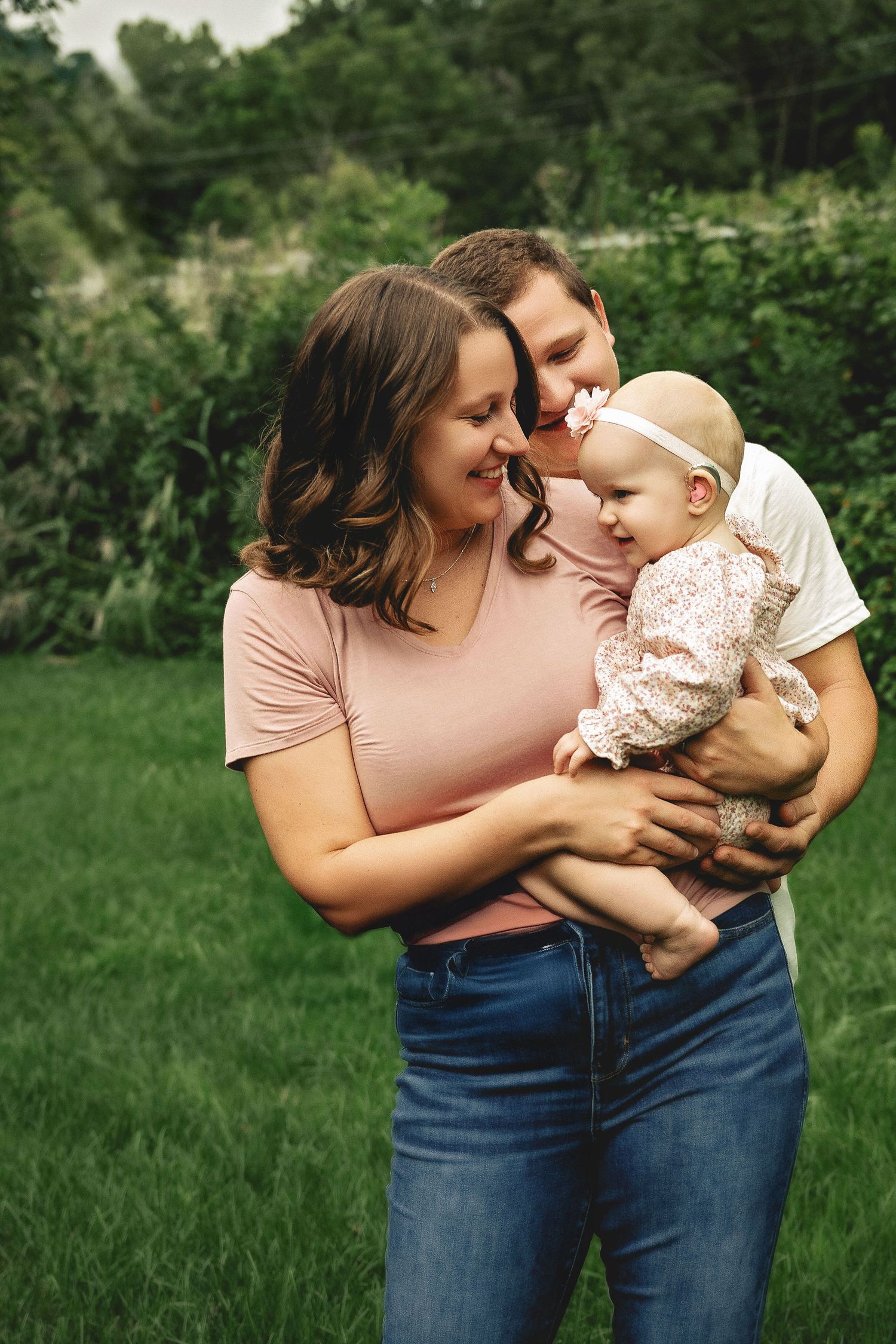 A tender family moment captured outdoors with a baby being held lovingly on a grassy lawn.