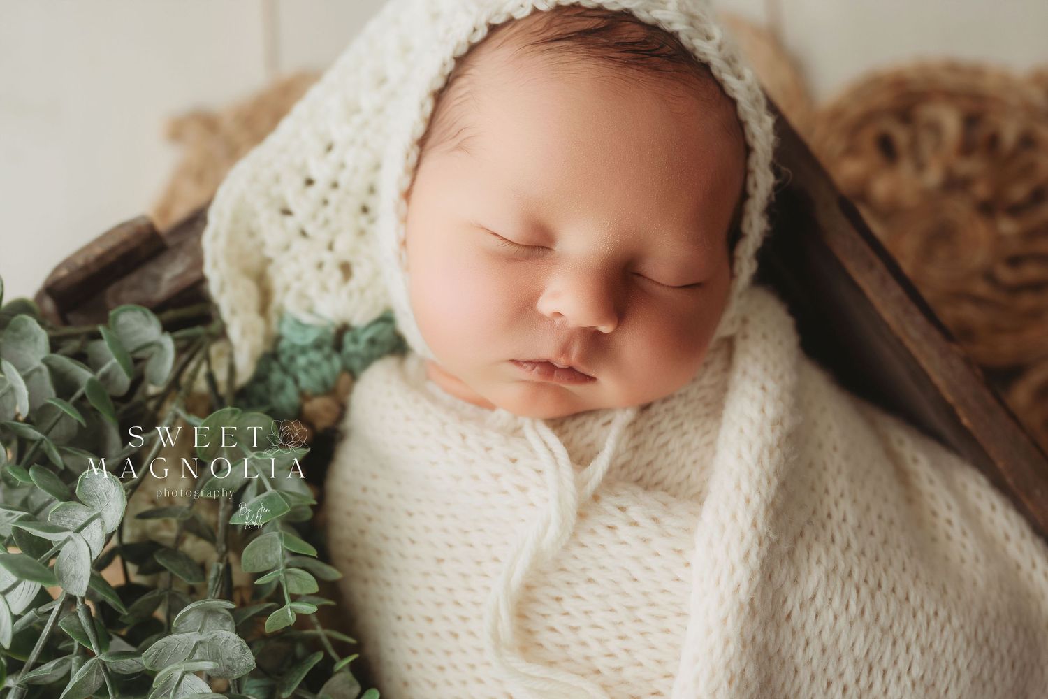 Artistic newborn portrait series with cream knit wrap and greenery accents.
