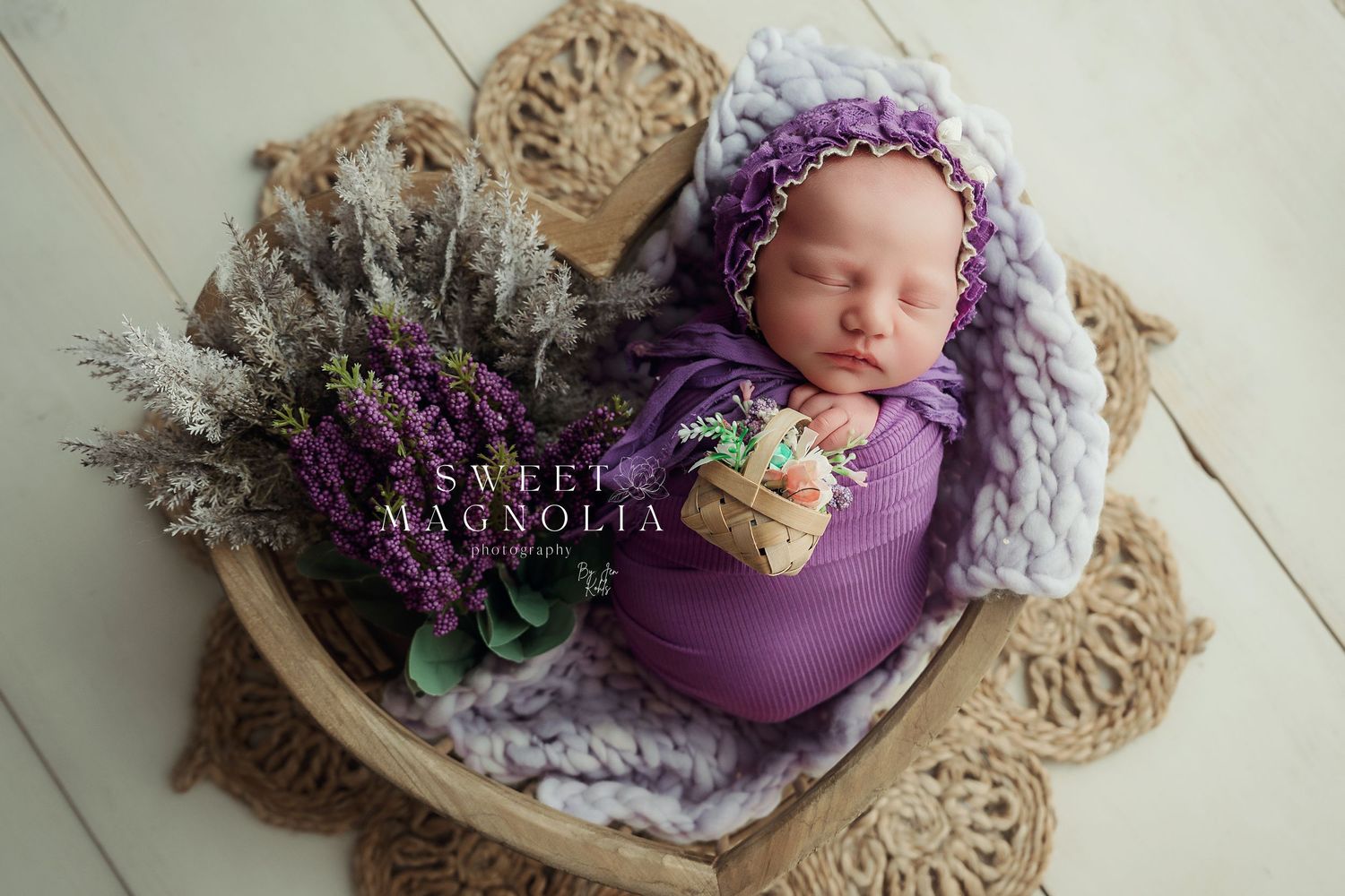 Newborn in purple wrap nestled in basket with lavender and floral decorations.