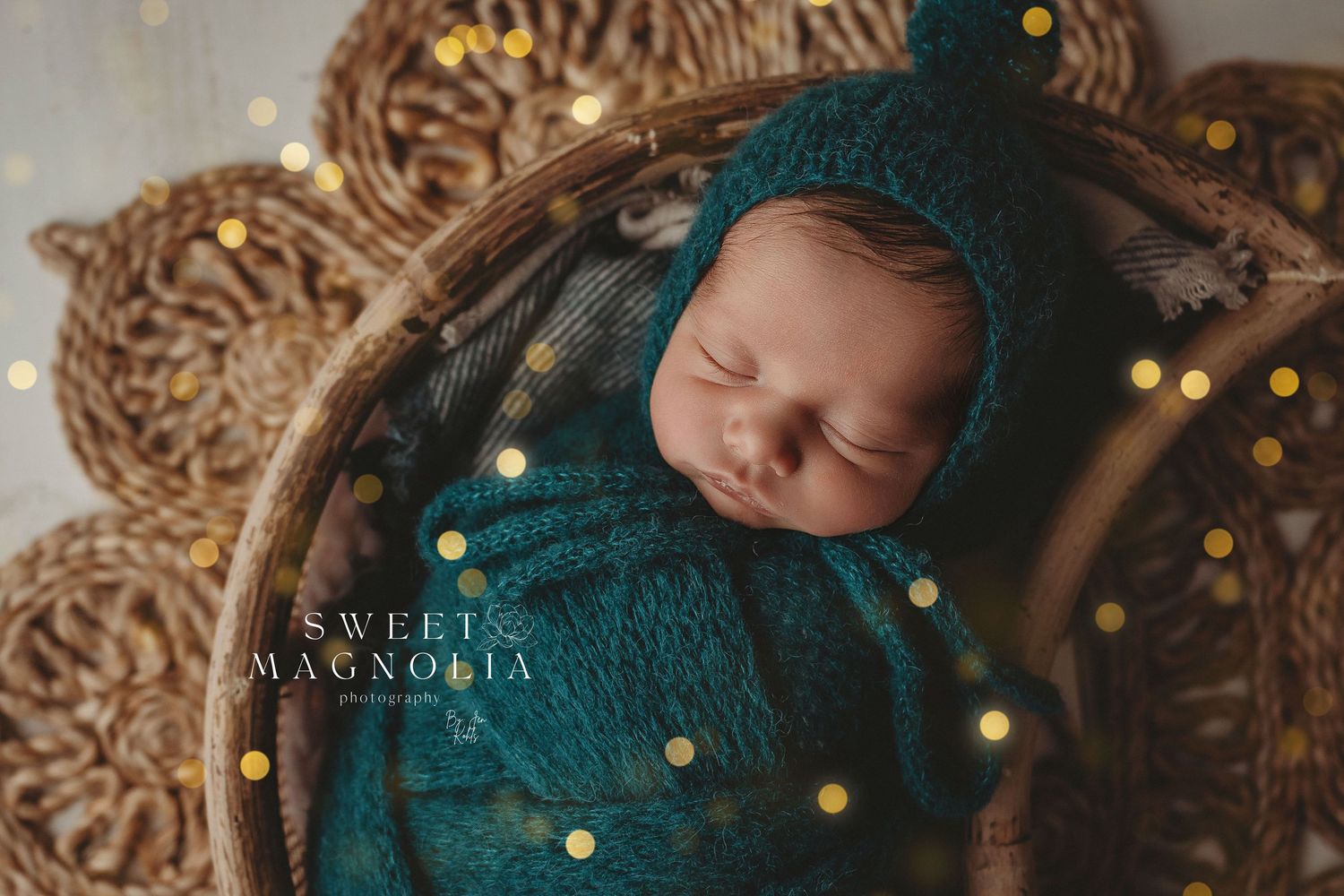 Dreamy newborn portrait with emerald wrap and sparkling golden bokeh effects.