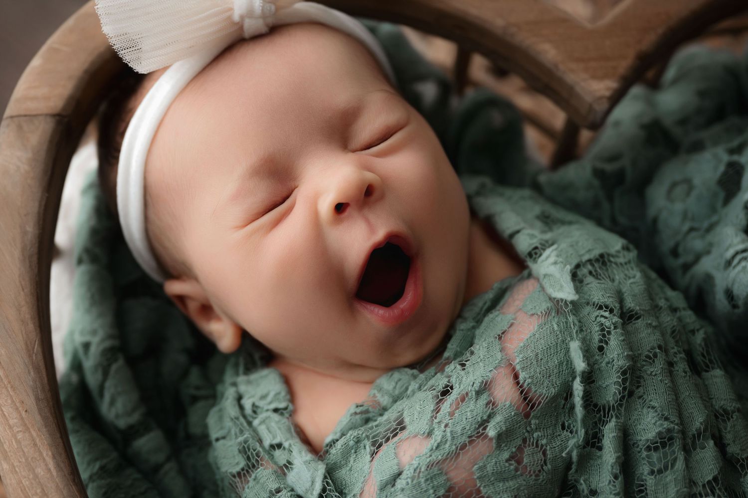 Sleeping newborn wrapped in teal blanket against textured background.