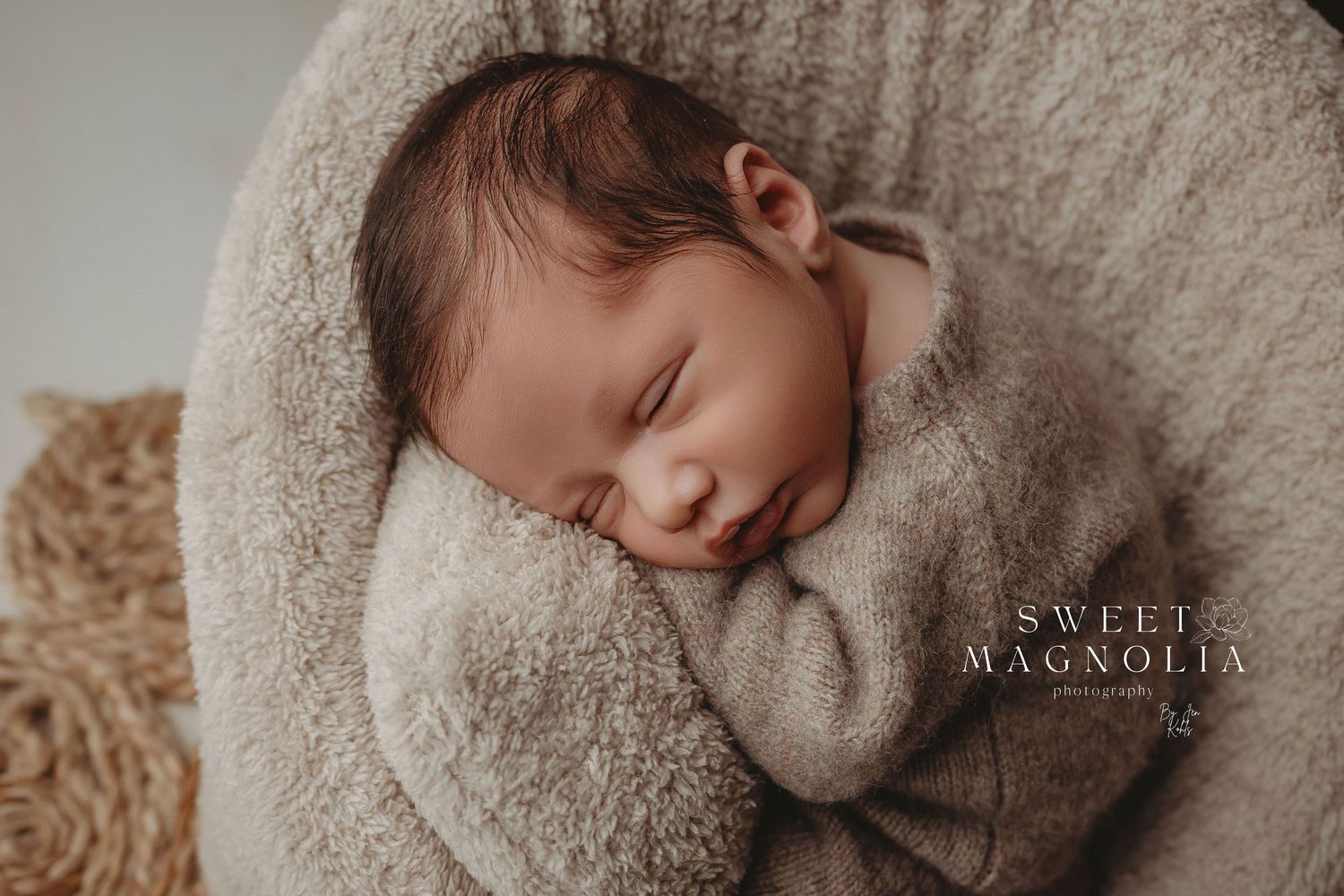 Sleeping newborn wrapped in cozy beige swaddle against neutral backdrop.