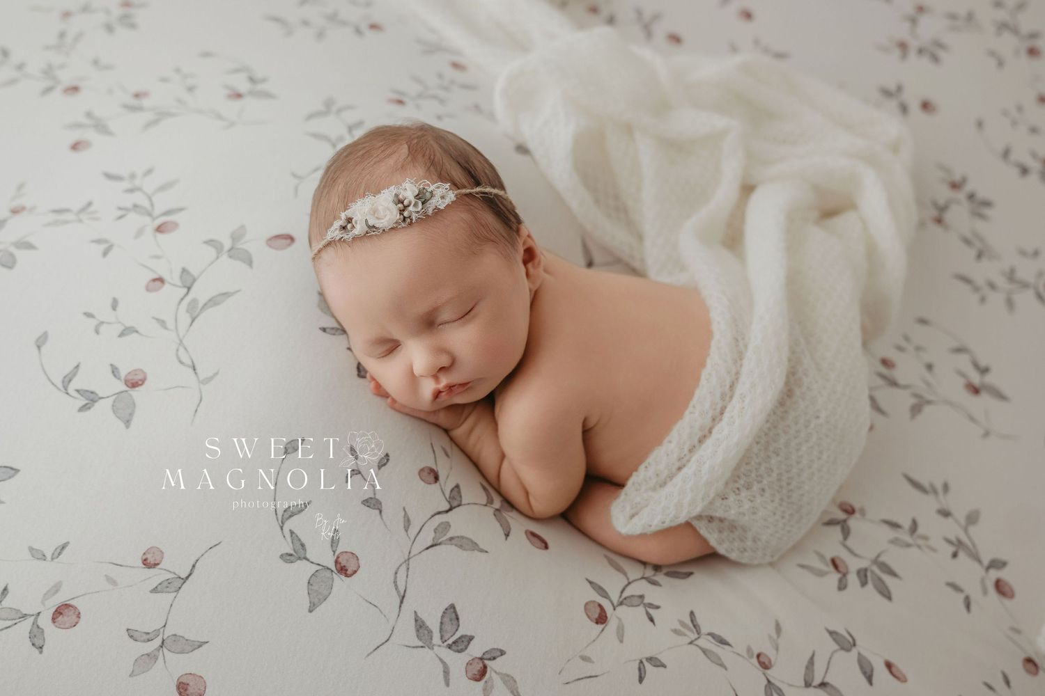 A peaceful newborn wearing a delicate headband sleeps on floral bedding.