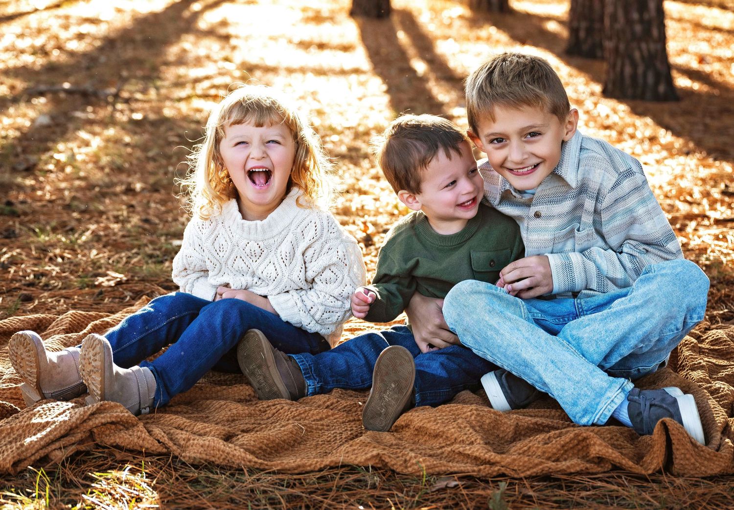 Children playing and laughing while lying on autumn leaves in dappled sunlight.