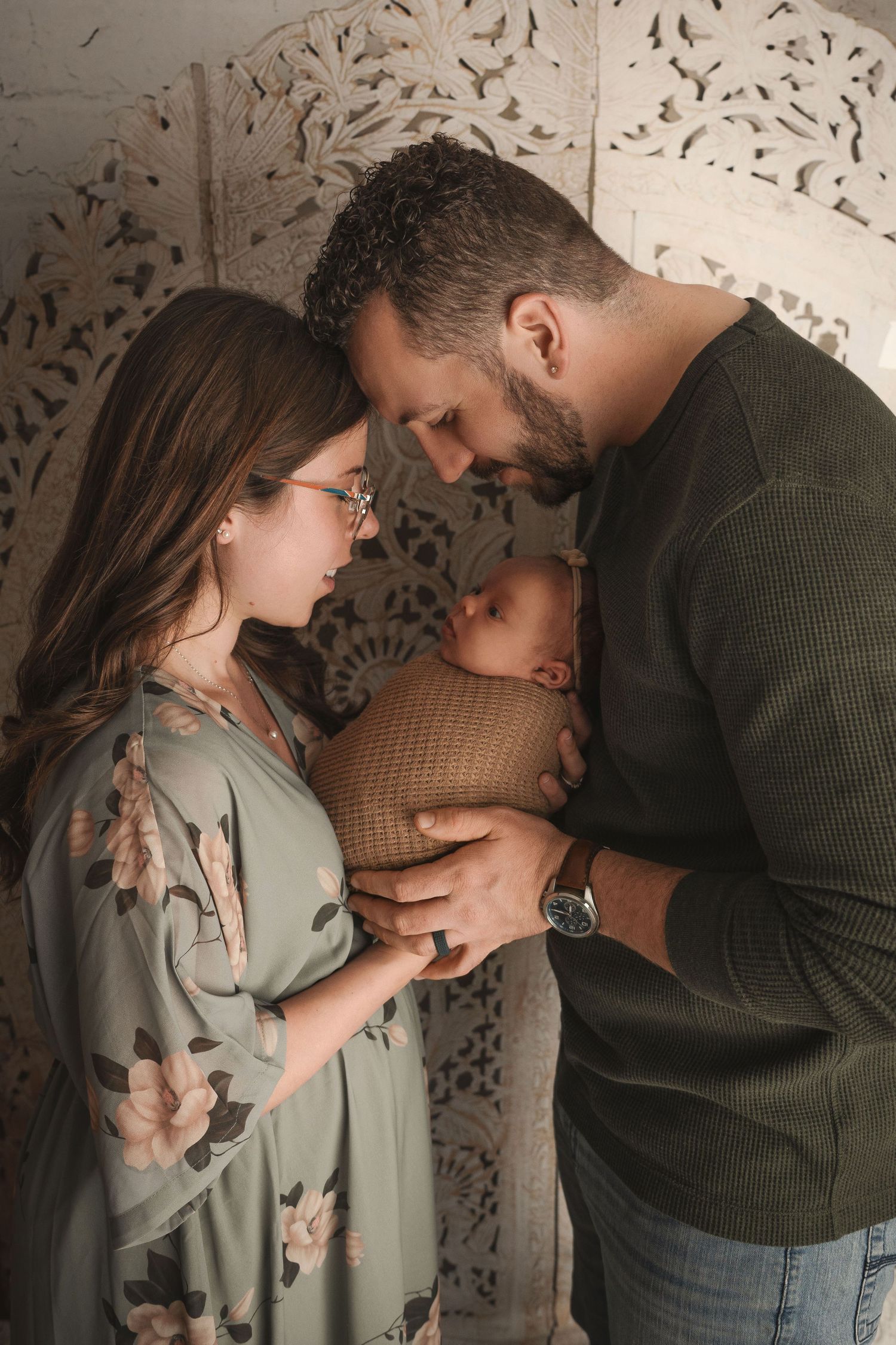 Intimate lifestyle portrait session with sage green dress against decorative wall backdrop.