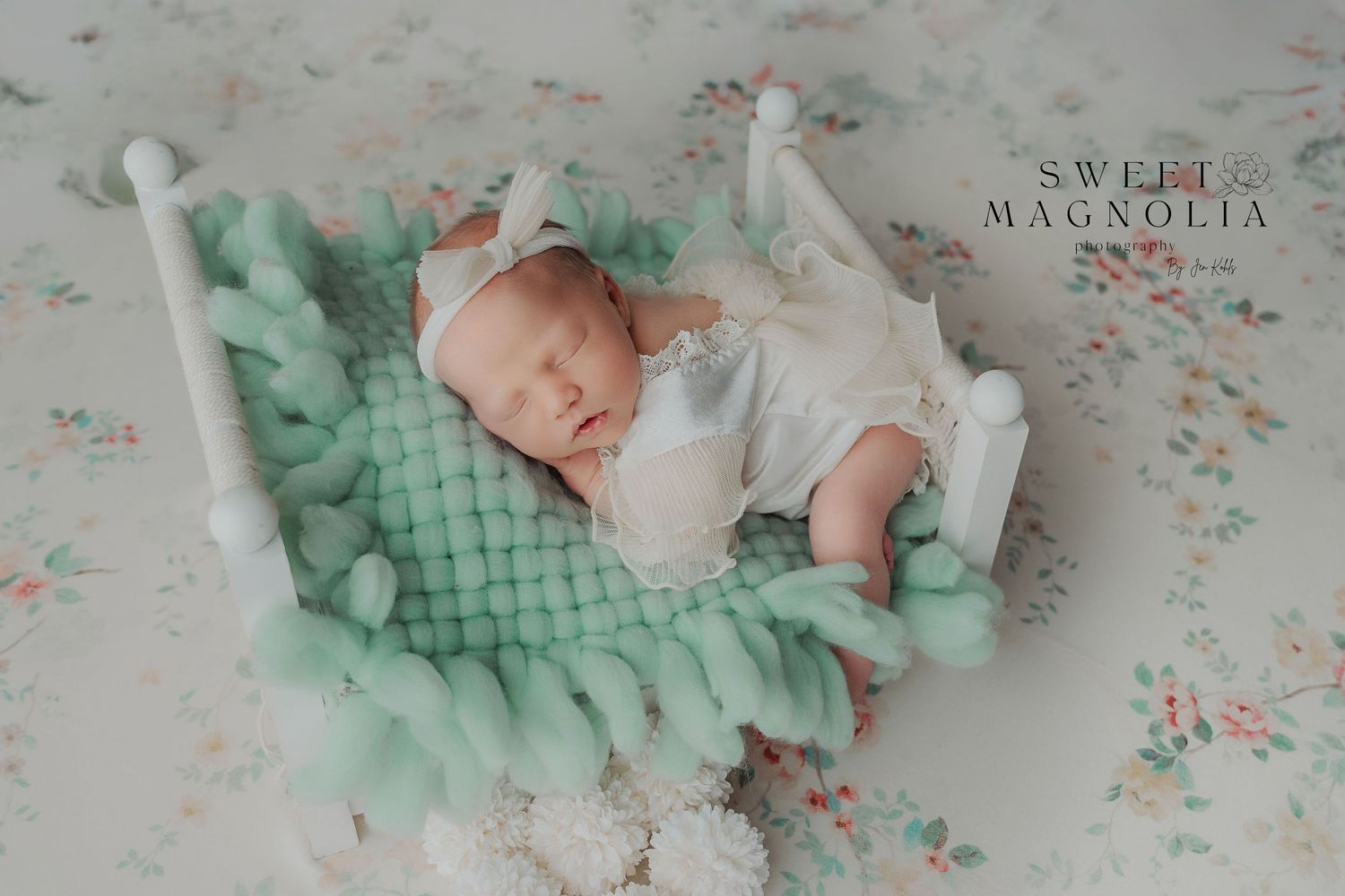 Sleeping infant on mint green textured blanket with white pom pom decorations.