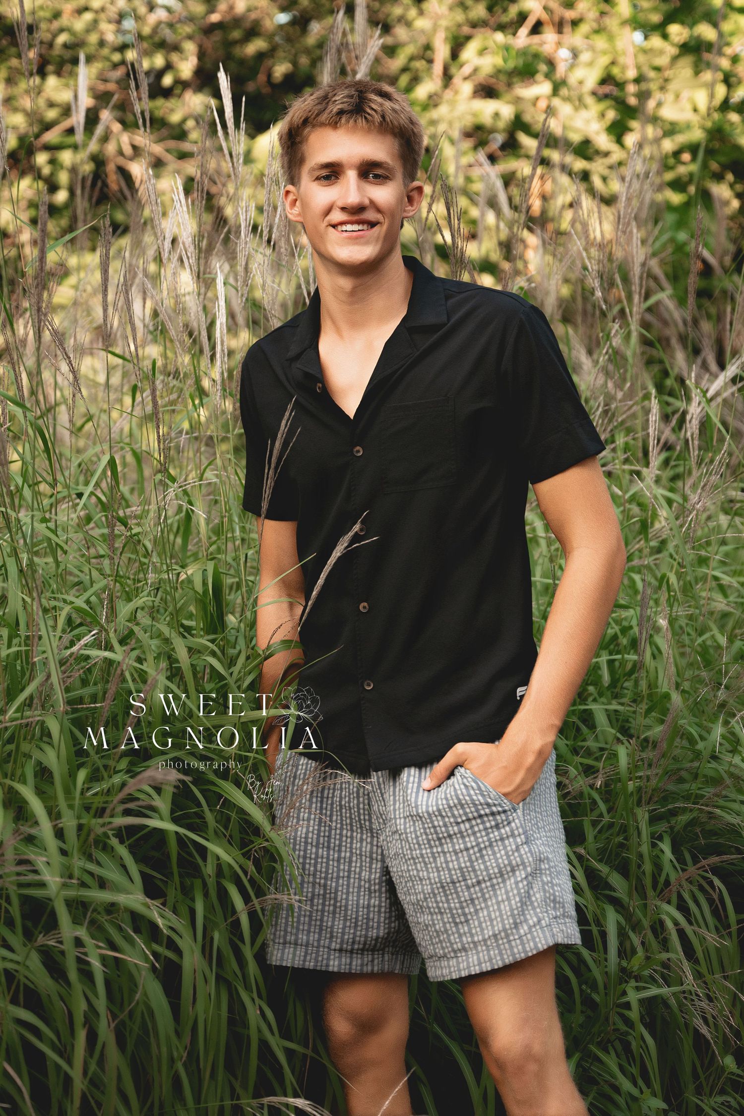 Summer portrait session in tall grass wearing black top and plaid shorts.