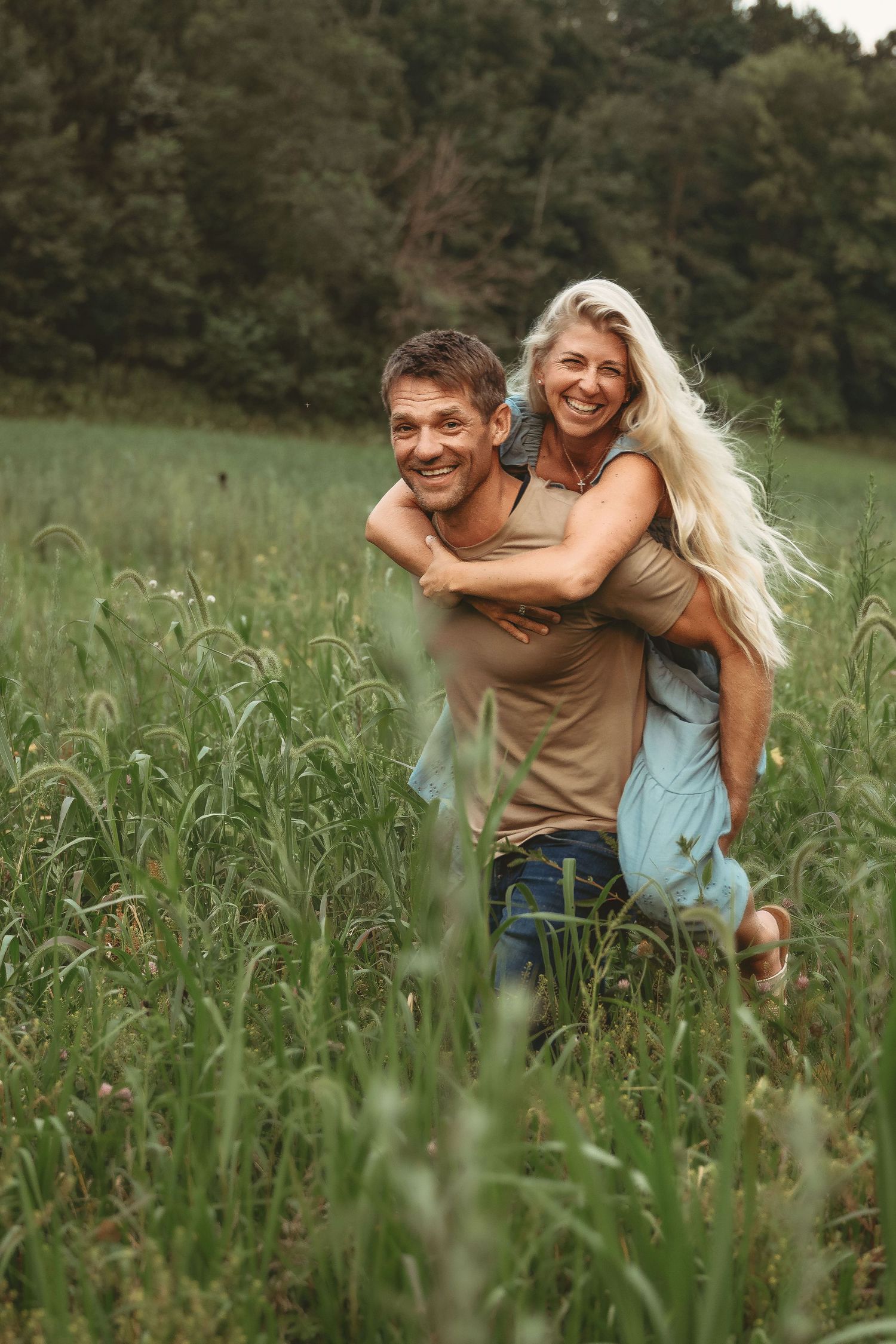Playful couple in casual clothes having fun in a tall grass field.