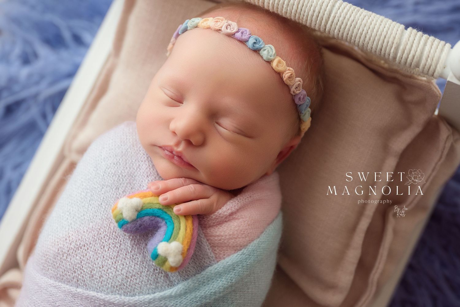 Sleeping newborn wrapped in soft pink swaddle with rainbow accessory and pastel headband.