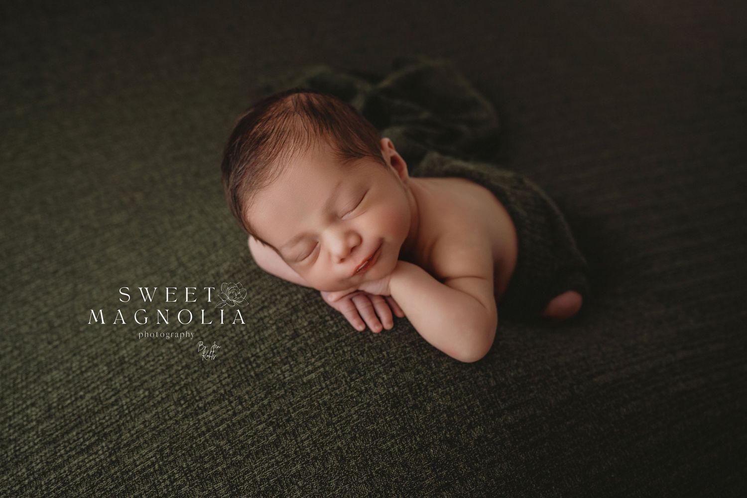 Artistic newborn portrait on dark green textured backdrop with minimalist styling.