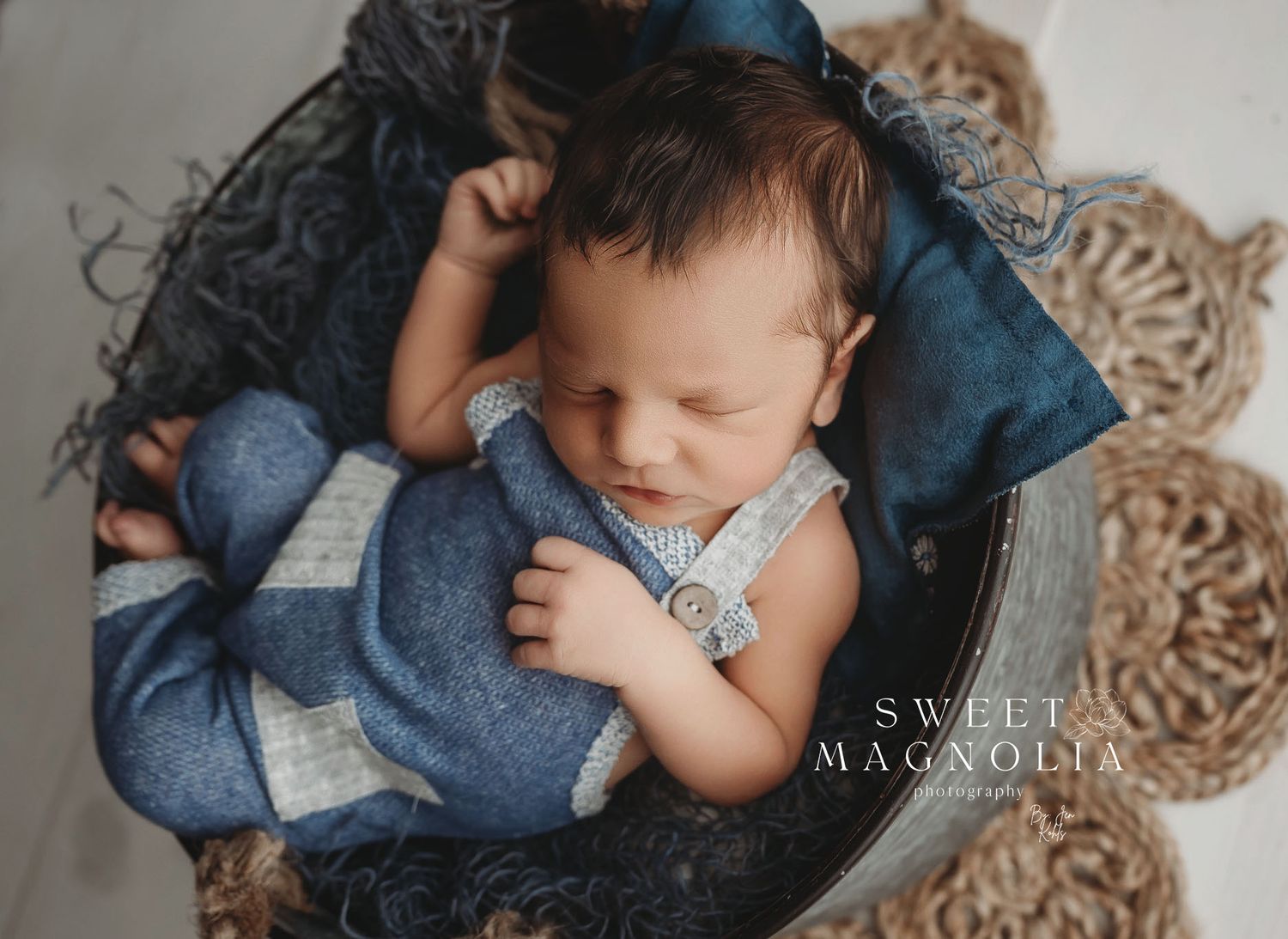A sleeping newborn wrapped in blue fabric on a textured backdrop.