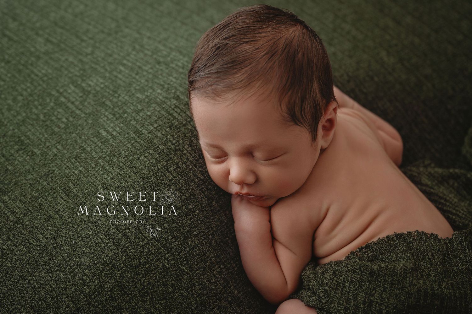 Peaceful sleeping newborn posed on deep green velvet fabric in studio setting.