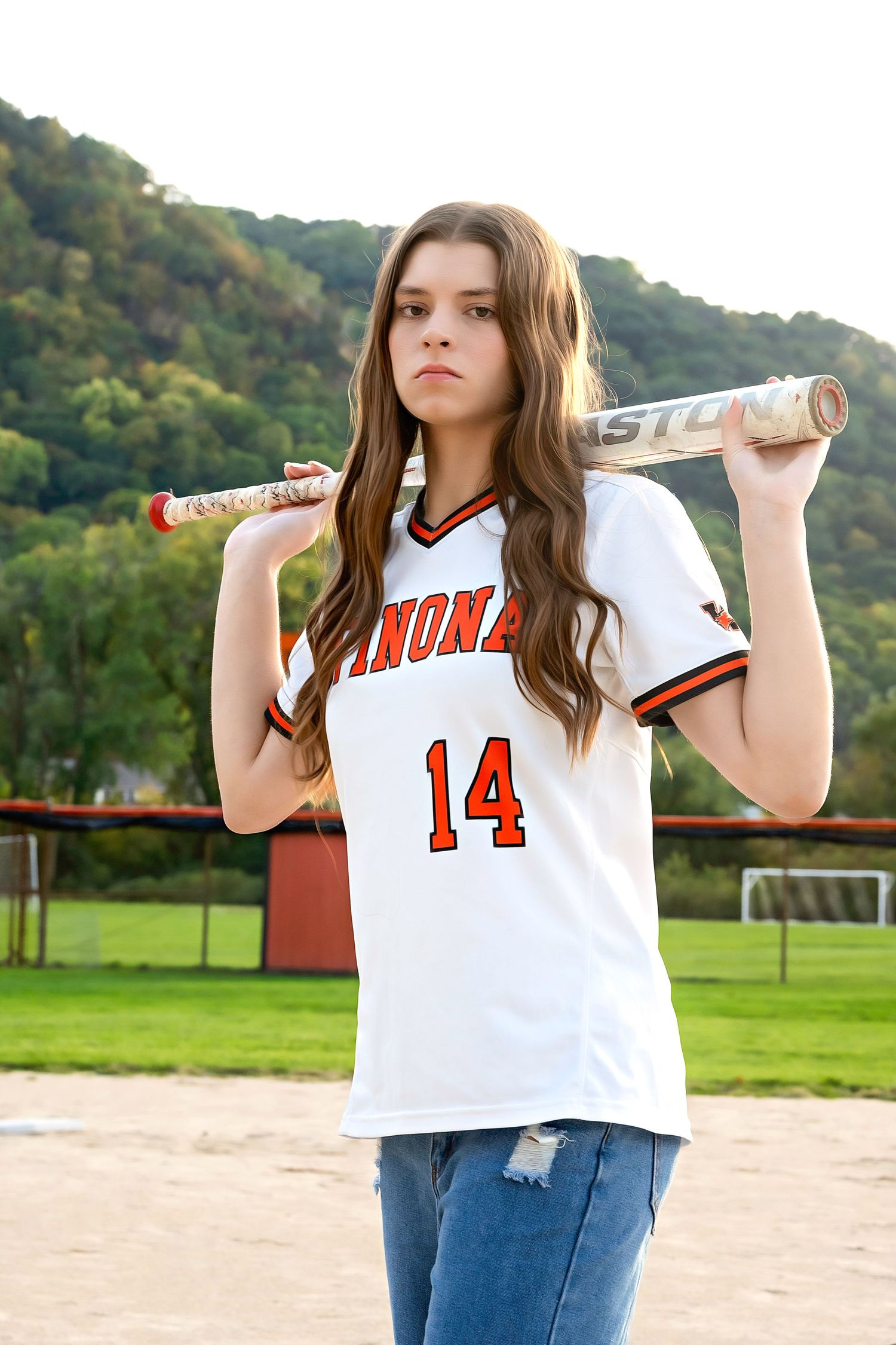 Sports themed photo shoot on a baseball field with white jersey and bat.