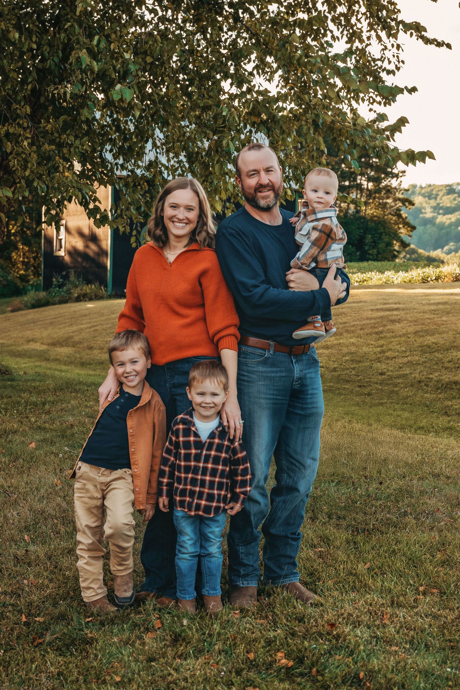 Family group photo outdoors on a grassy hill during golden hour.