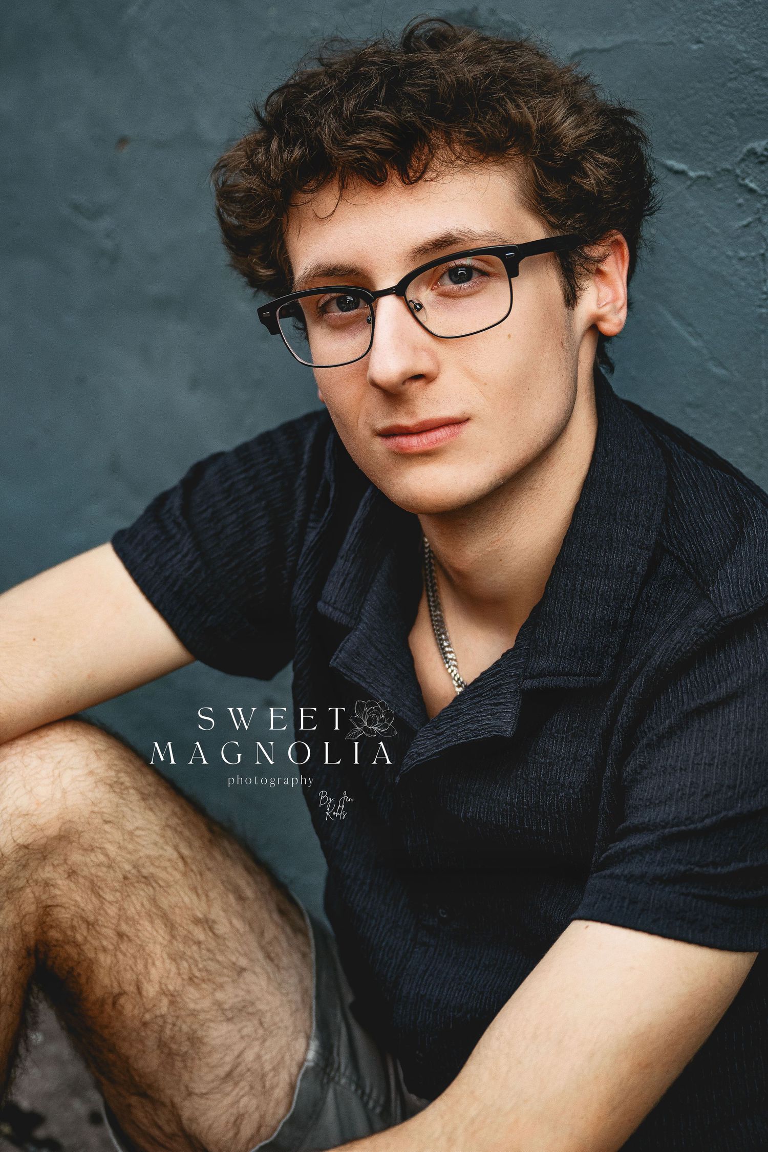 Portrait series against dark wall featuring casual black shirt and glasses styling.