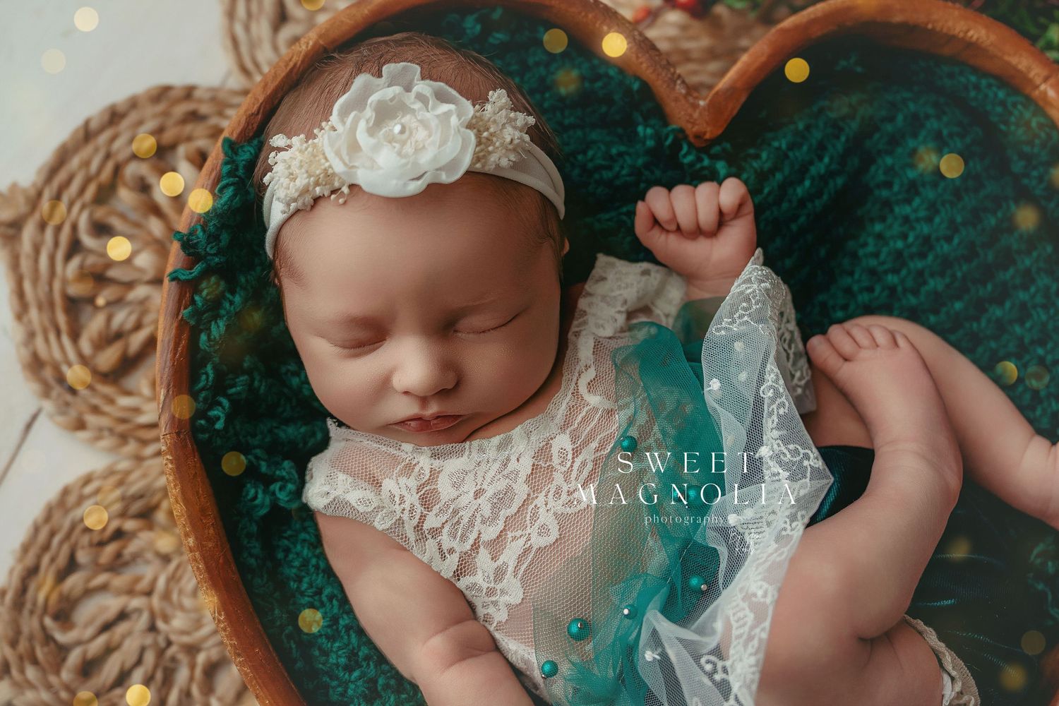 Artistic newborn portrait with teal blanket and twinkling bokeh lights creating magical atmosphere.