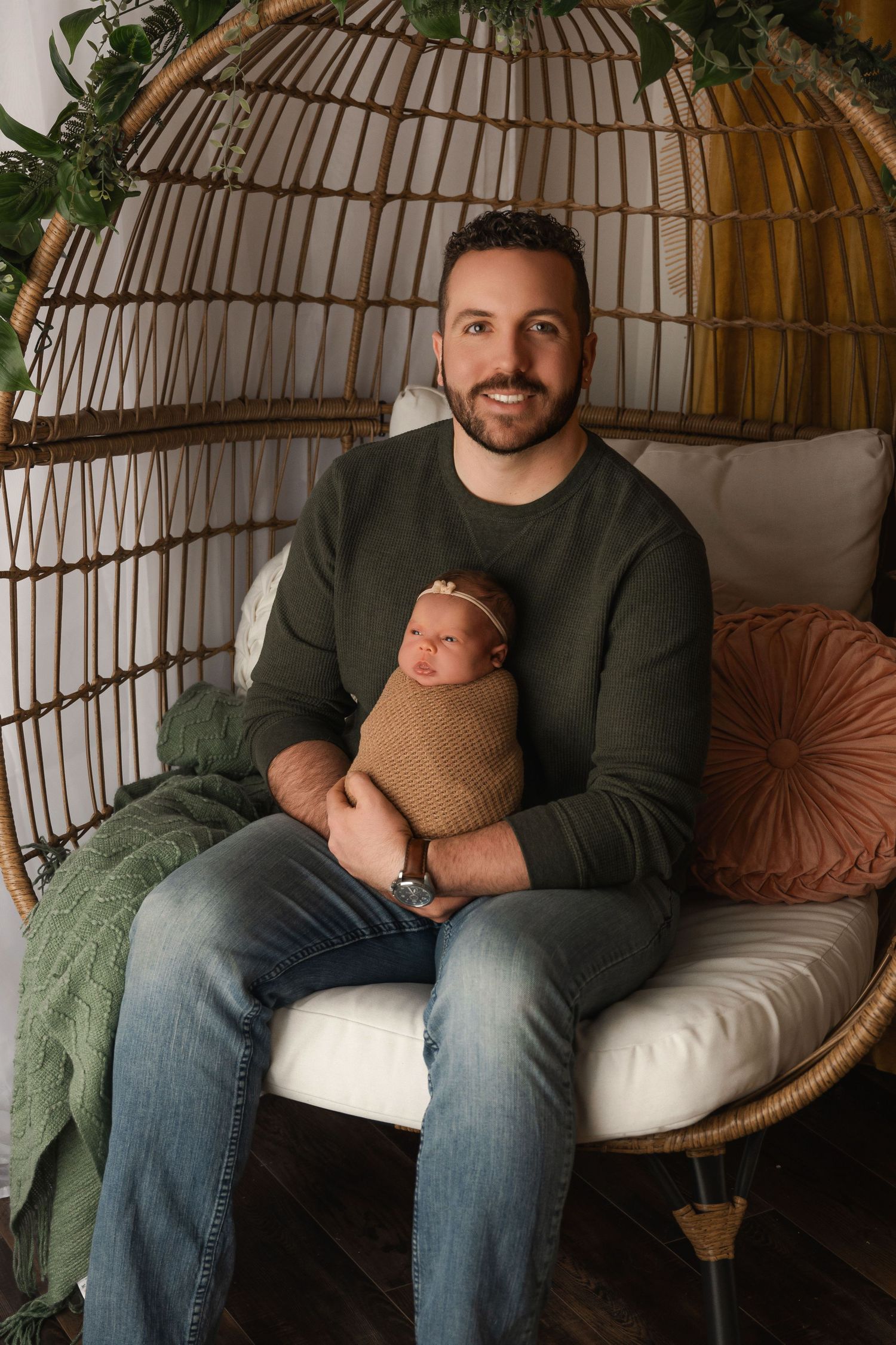Cozy portrait session in hanging rattan chair with green plants and cushions.