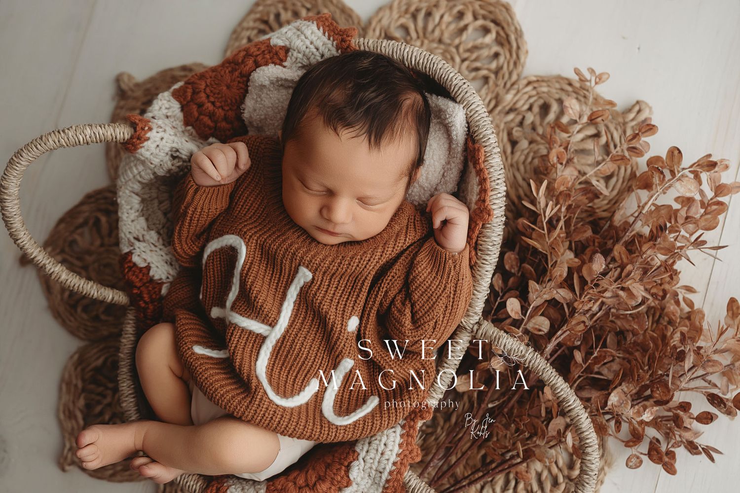 Newborn in rust-colored knit outfit sleeping on macrame and woven textures.