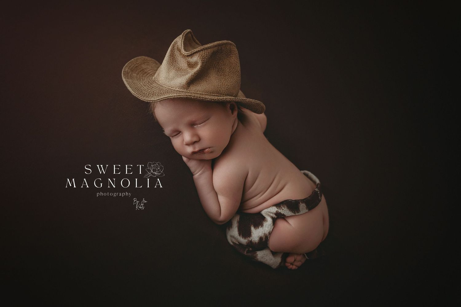Dramatic low-key newborn photography with dark background and artistic lighting.