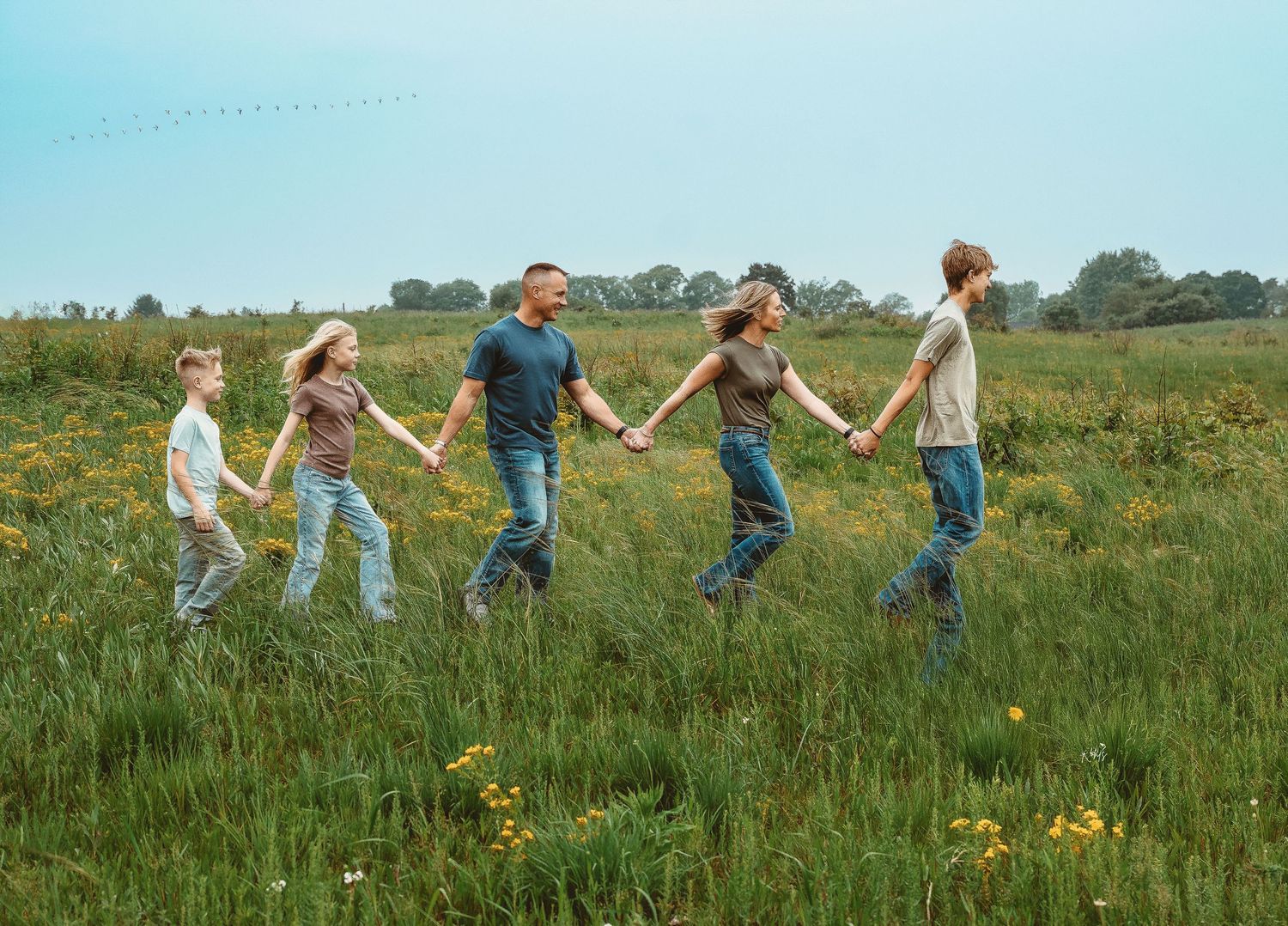 People walking hand in hand through a sunny meadow with wildflowers.