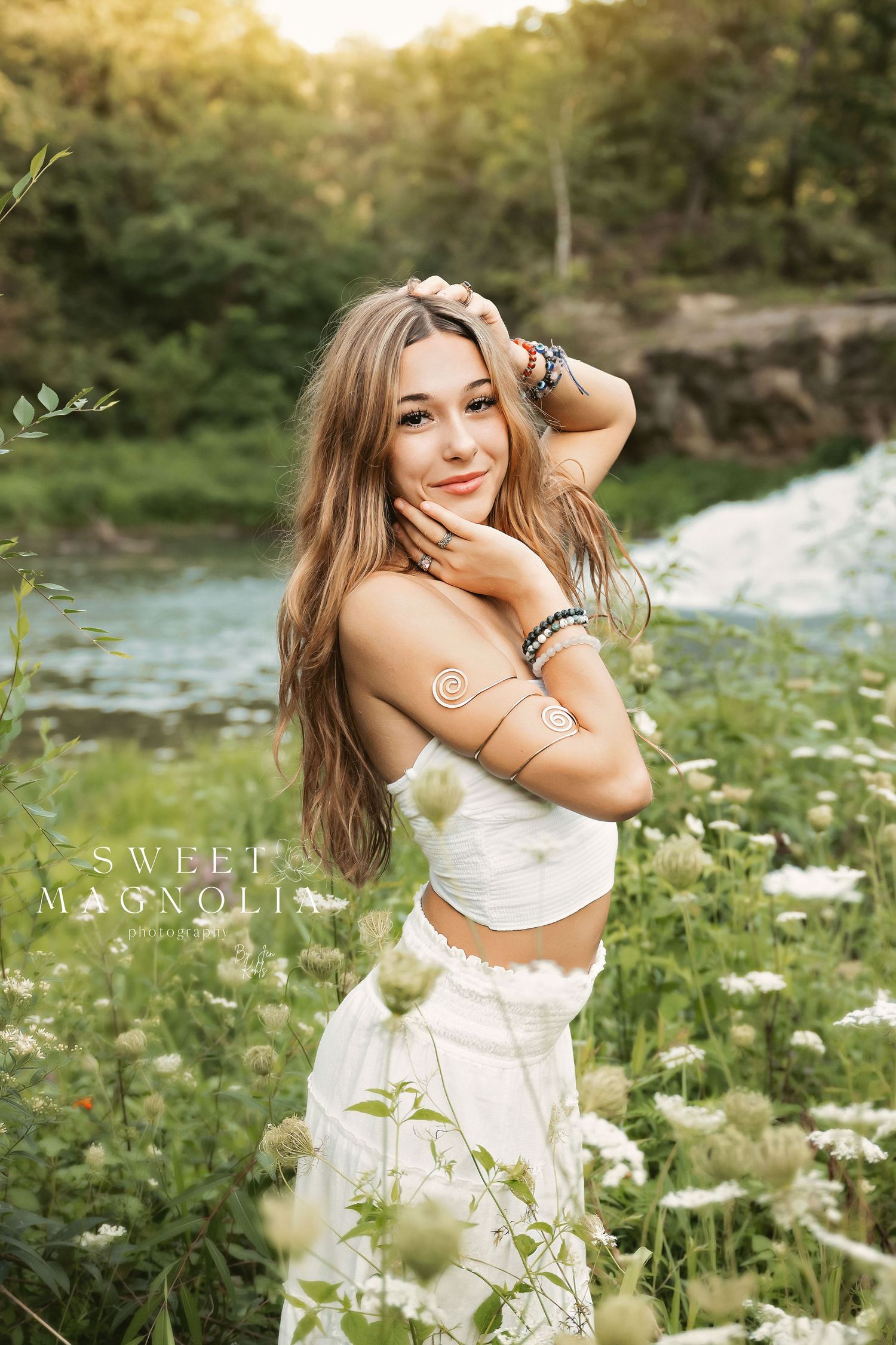 Young woman in white dress poses playfully in a sunny wildflower meadow.