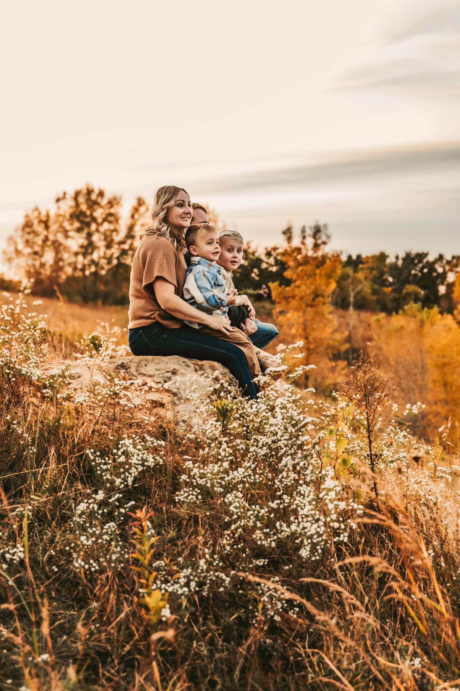 Family sitting together in a golden wildflower field at sunset.