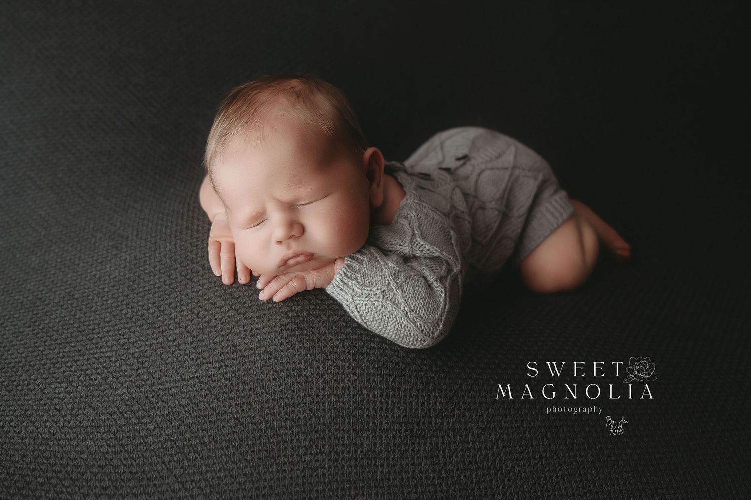 Newborn baby sleeping peacefully in dark moody lighting wearing a soft knit sweater.