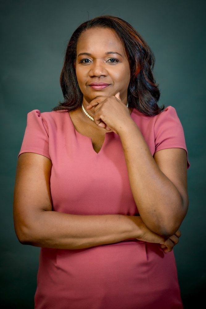 Professional portrait of someone in a pink top posing thoughtfully against a dark green background.