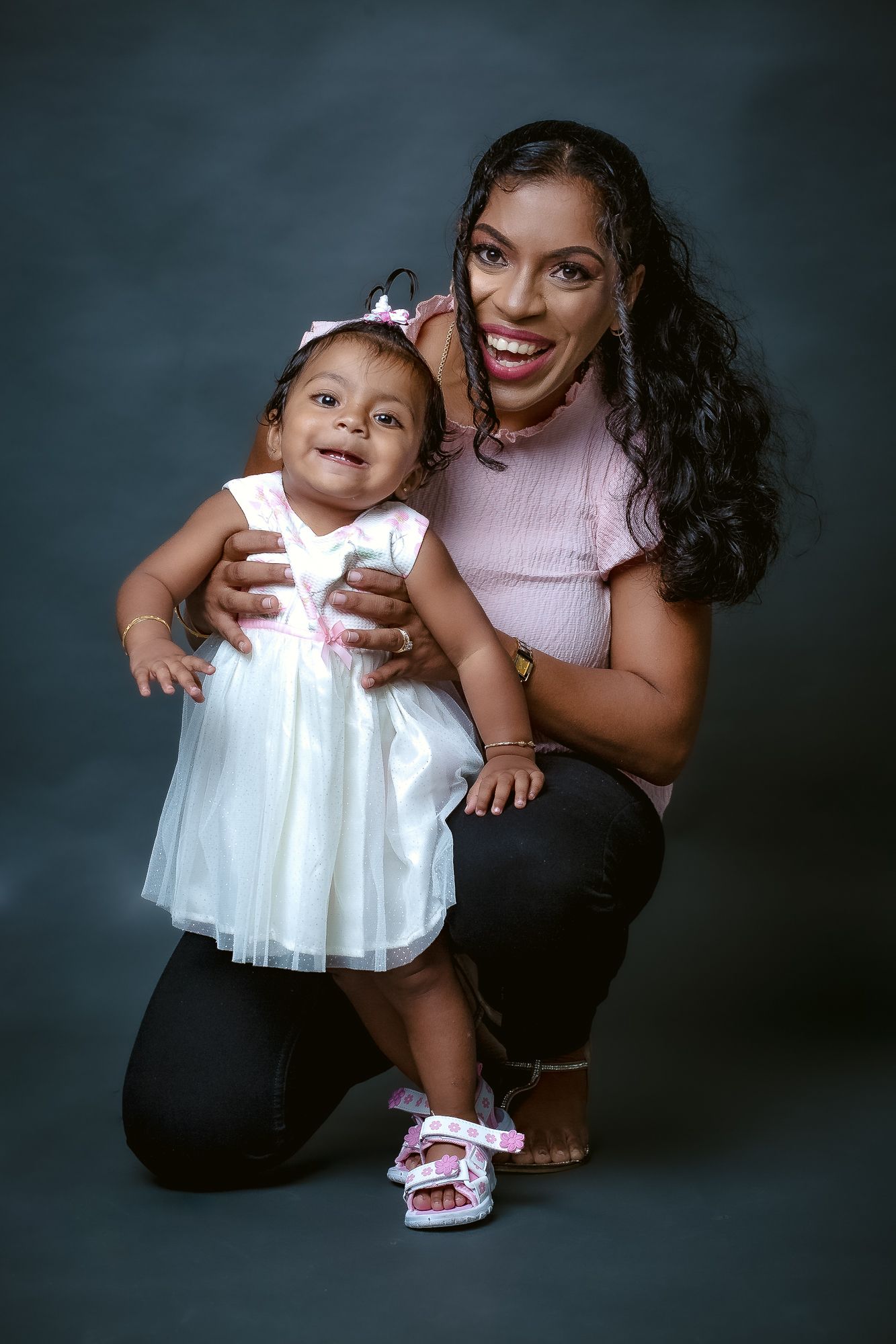 A heartwarming mother-daughter portrait with the child wearing a white dress and sparkly shoes.