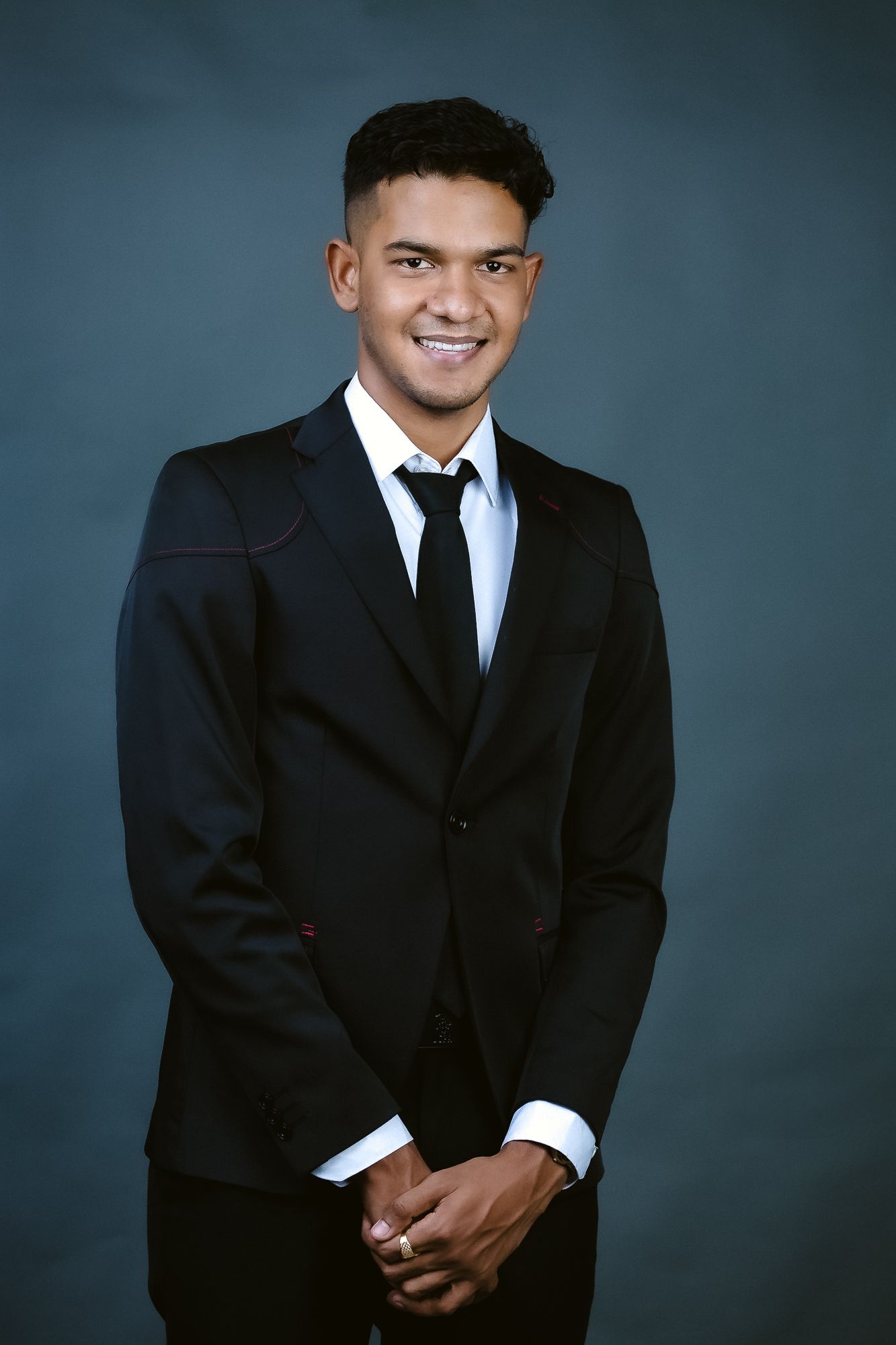 Professional studio portrait of a person in a black suit and tie against a blue background.