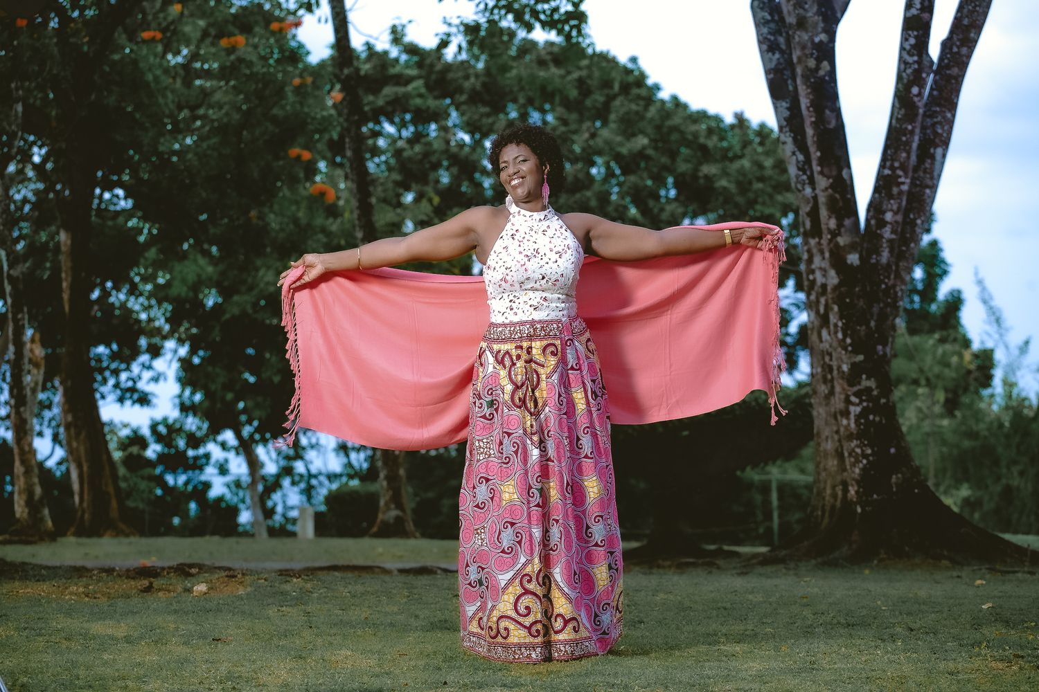 Someone wearing a colorful floral skirt and white top poses outdoors while holding up a coral-colored fabric.