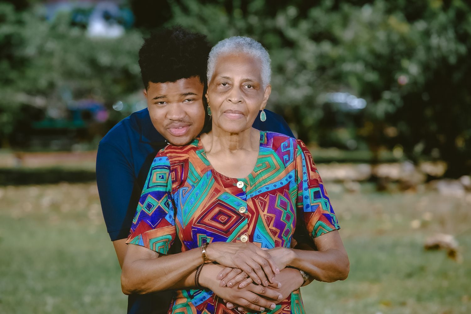 An emotional embrace between two people outdoors with one wearing a colorful geometric print top.