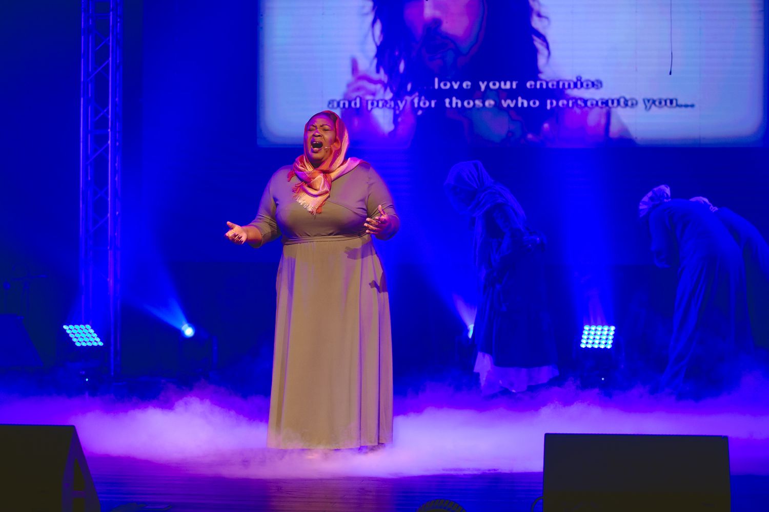 Solo performer singing on a misty stage illuminated by blue theatrical lighting.