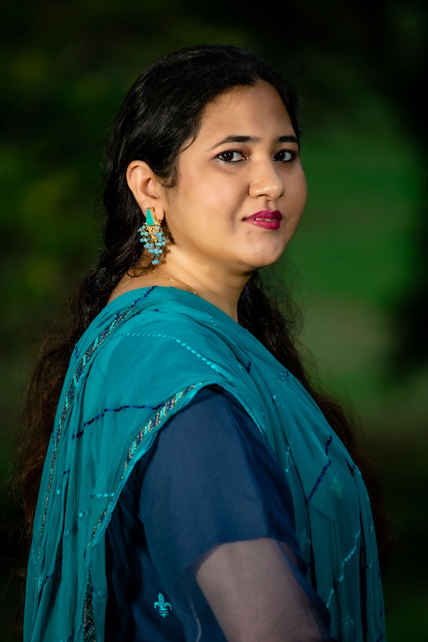 Portrait of woman in traditional blue and teal South Asian attire with turquoise earrings.