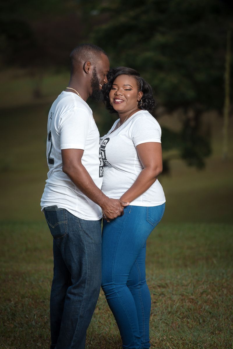 Couple wearing white t-shirts sharing an intimate outdoor moment in a grassy field with trees in the background. Palmiste Park, Trinidad