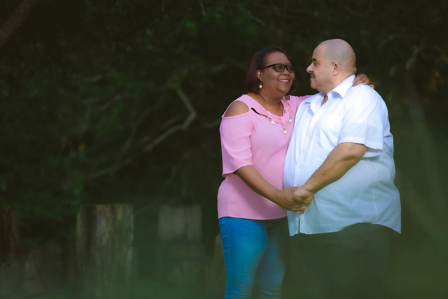 A couple shares an intimate moment together outdoors in casual attire against a dark green background.